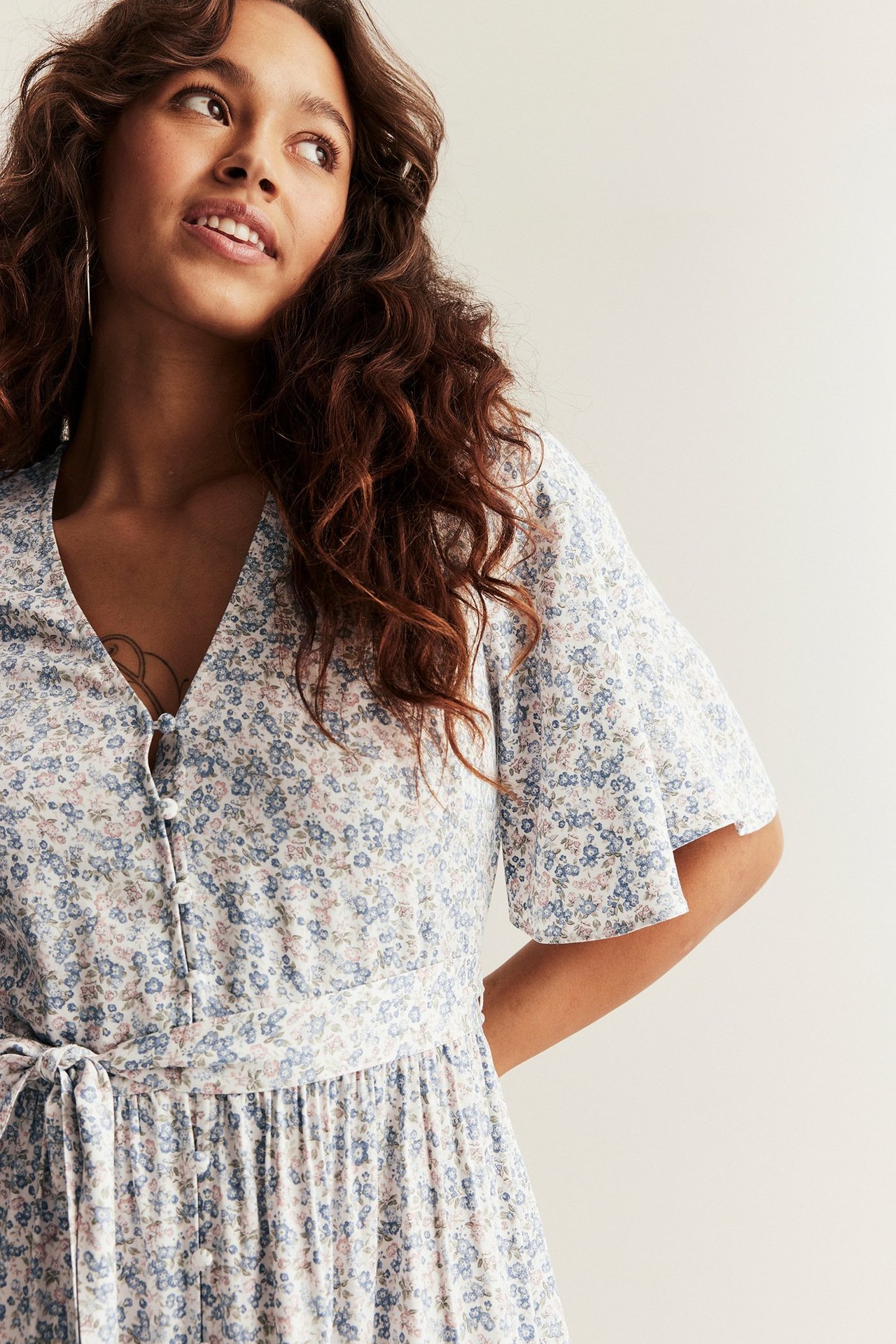 Nahaufnahme frontal einer Frau in offwhite Blumenmuster Viskosekleid mit V-Ausschnitt, kurzen Ärmeln und Gürtel.