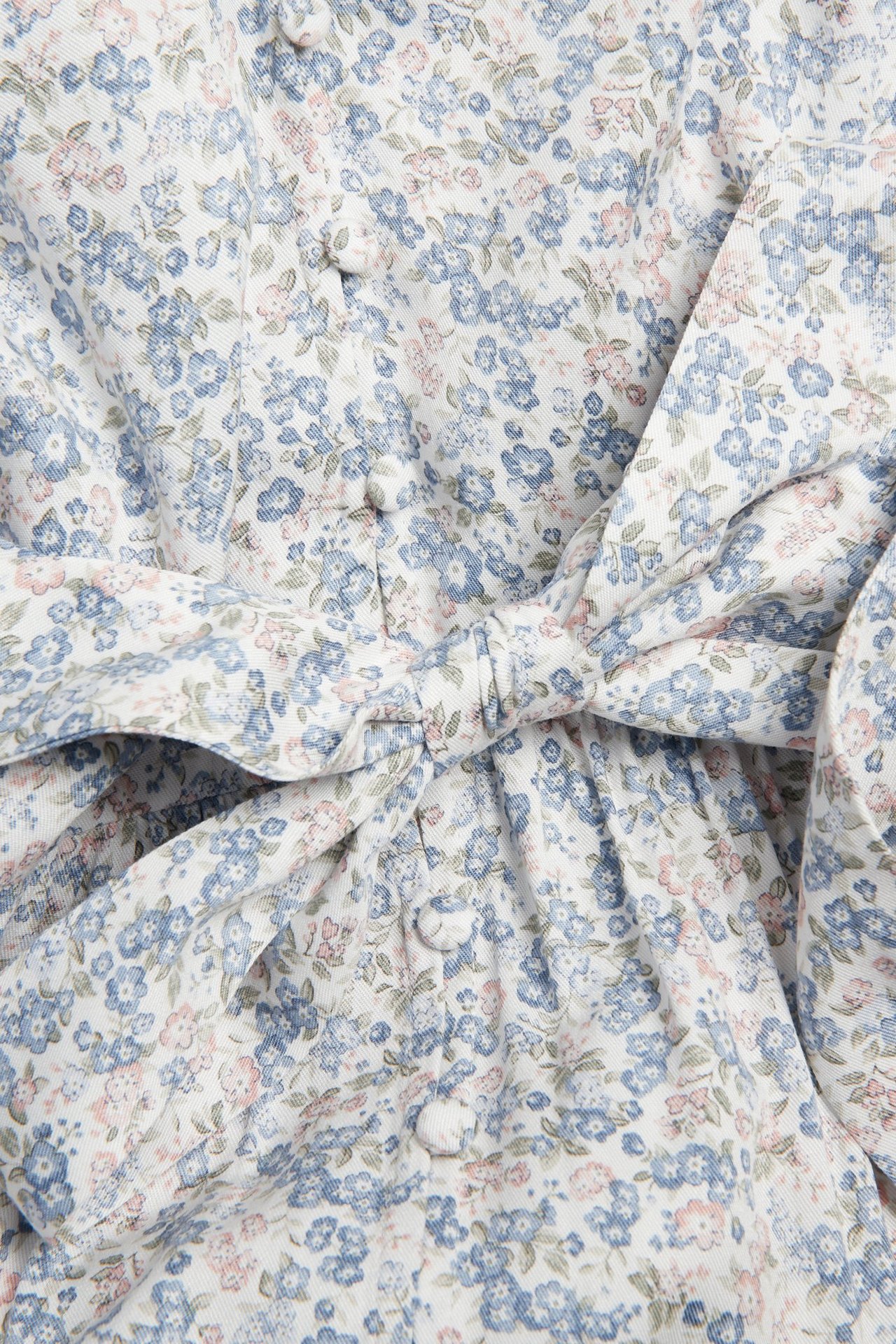 Close-up of an off-white floral viscose dress with blue and pink flowers, covered buttons, and a matching knotted belt.