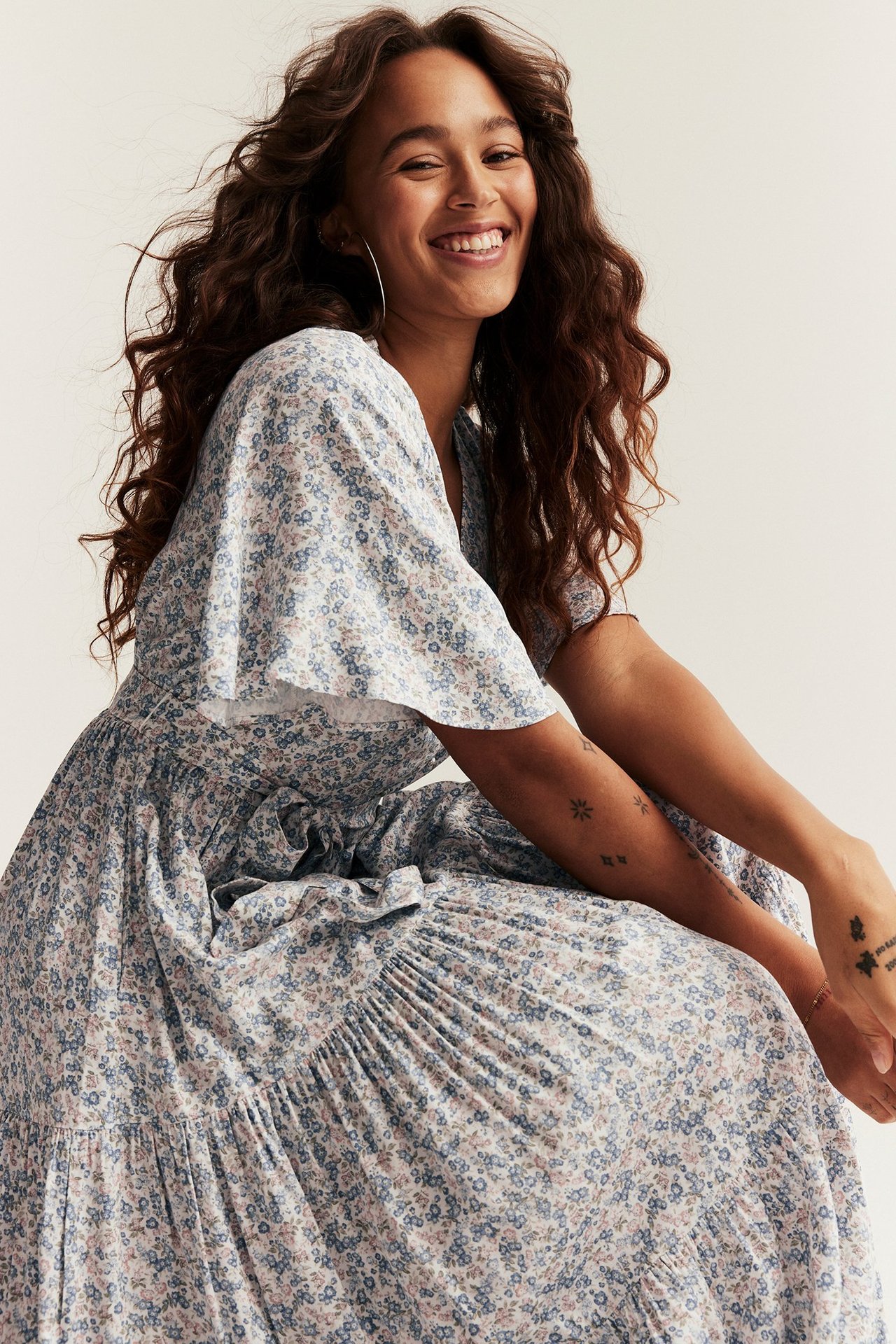Front view of a smiling woman wearing an off-white floral viscose V-neck dress with short sleeves and a tied waist.