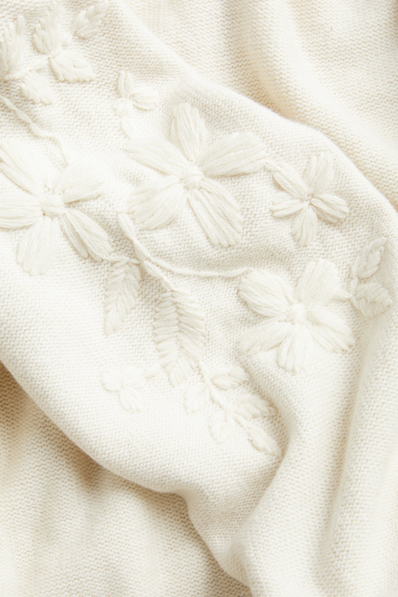 Close-up of a cream knitted fabric with raised floral embroidery.