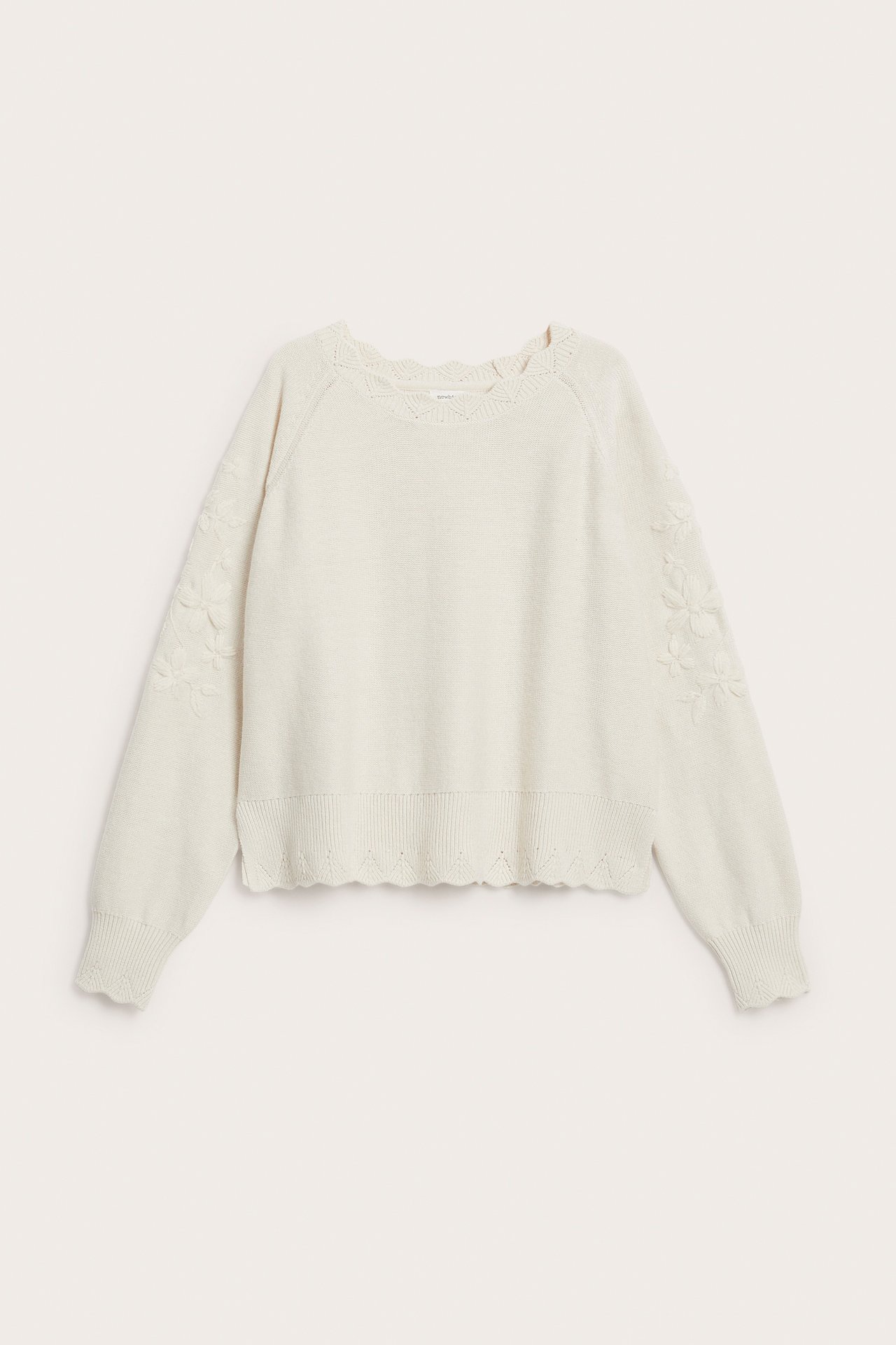 Front view of a cream knitted sweater with scalloped edges and floral sleeve embroidery.