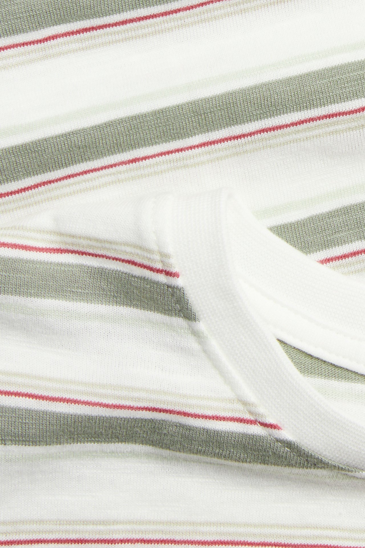 Nahaufnahme eines offwhite Baumwoll-Slub-T-Shirts mit salbeigrünen, beigen und roten Streifen.