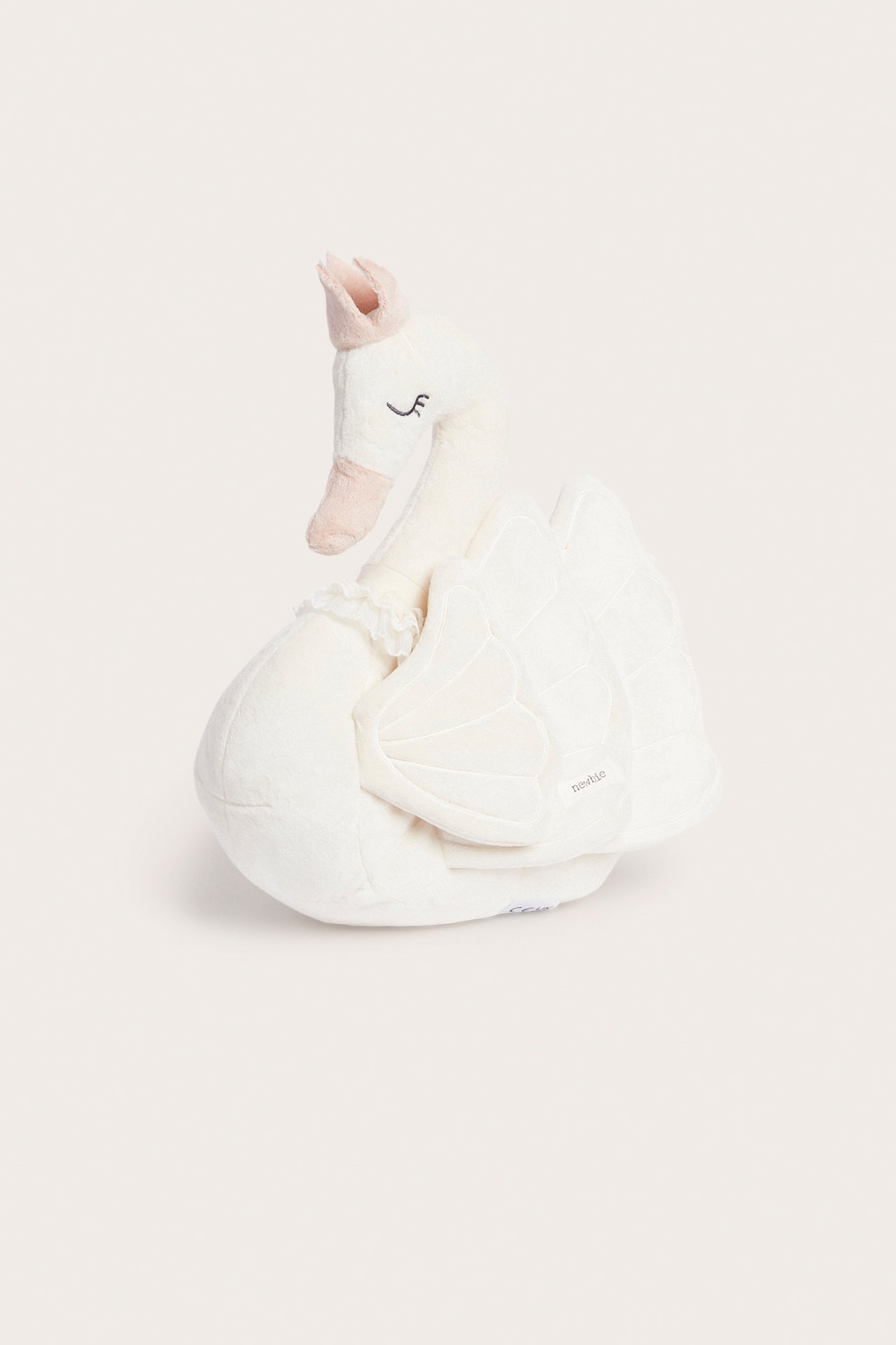 Front view of an off-white, soft swan-shaped plush pillow with a pink crown.