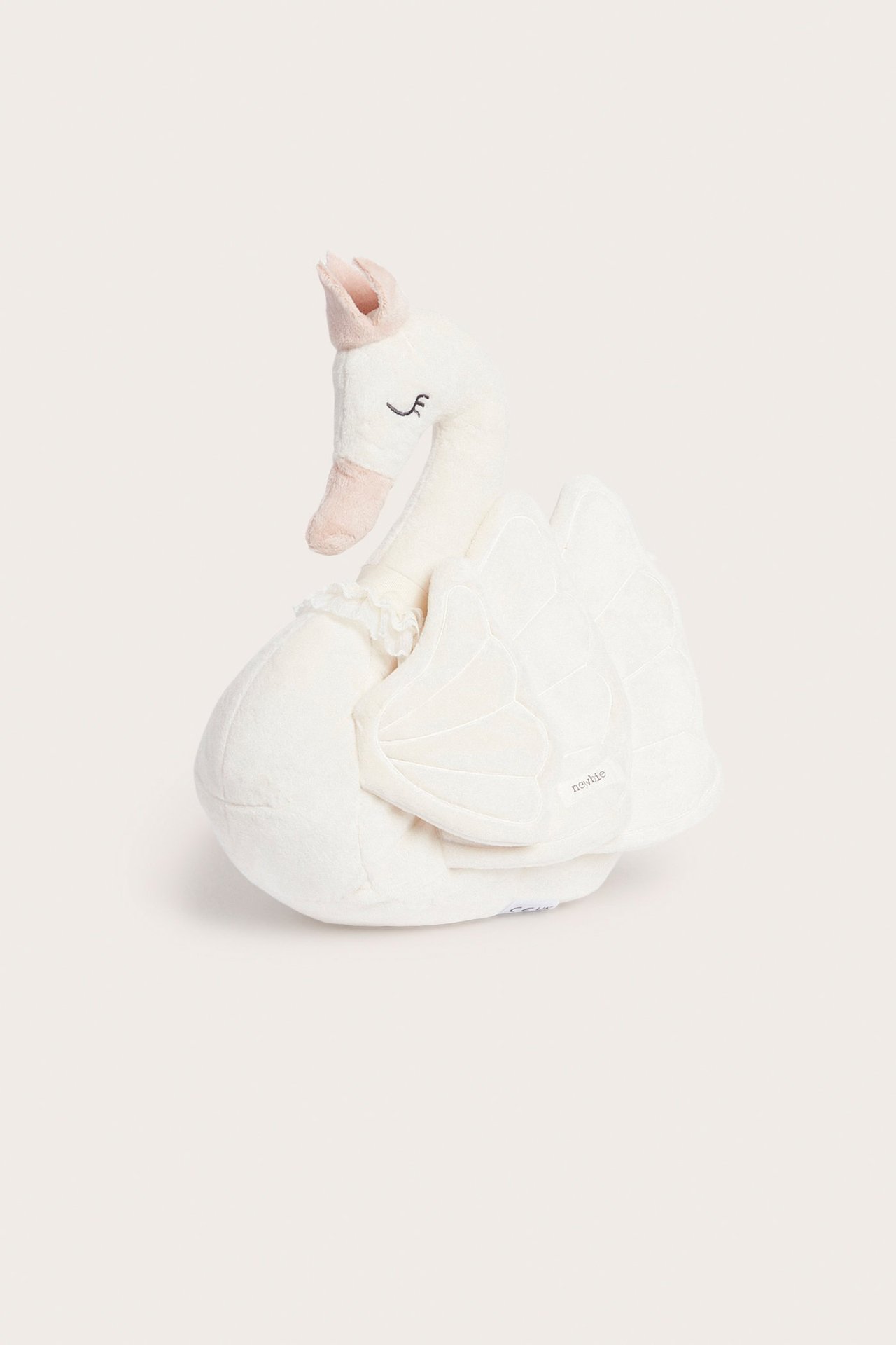 Vorderansicht eines cremeweißen, weichen, schwanenförmigen Plüschkissens mit einer rosa Krone.