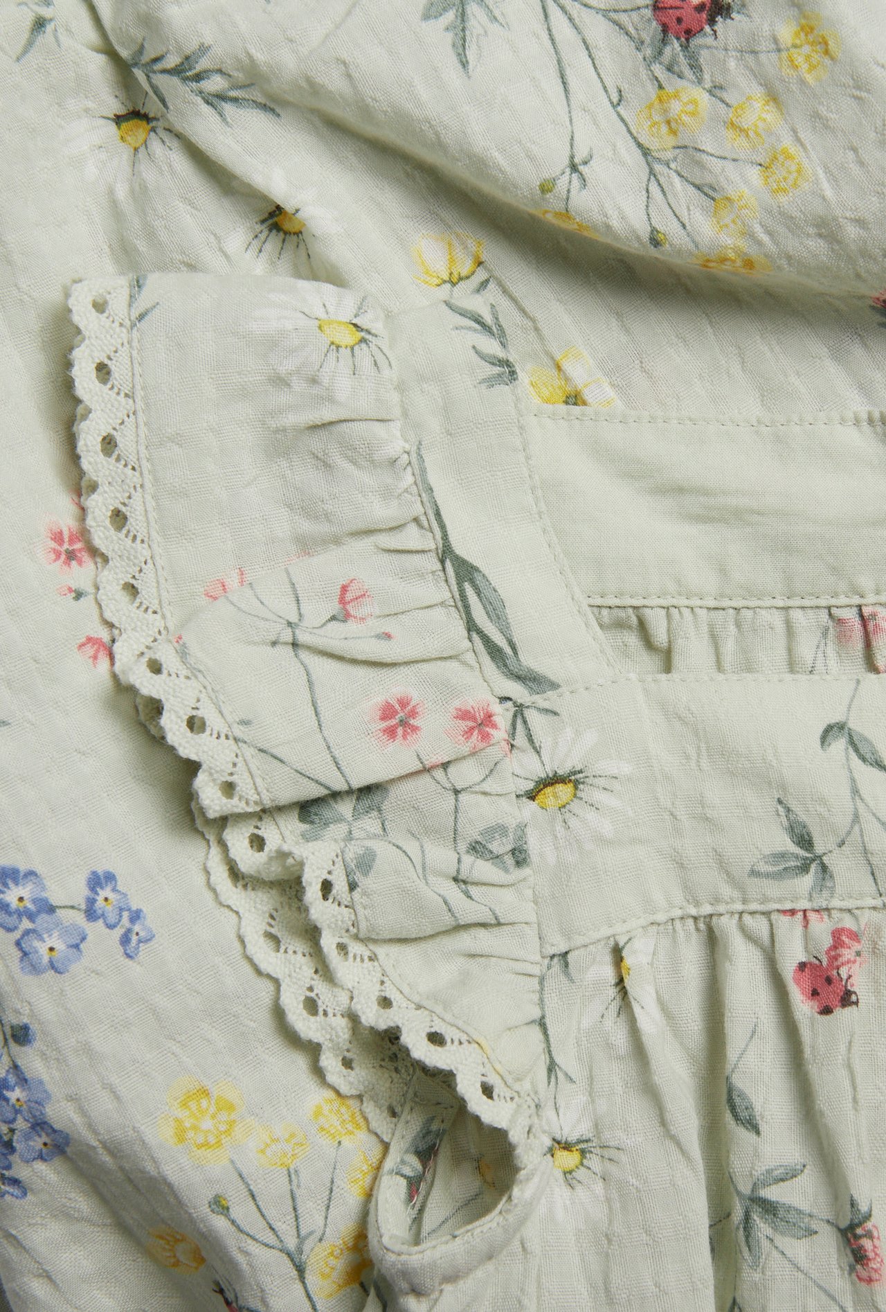 Close-up of a light green woven cotton romper with a floral pattern and ruffle sleeve with lace edge.