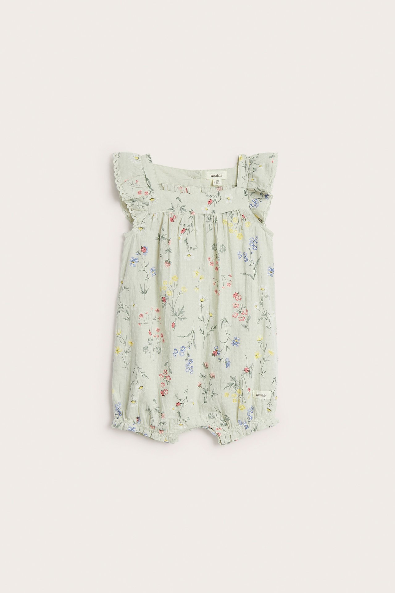 Front view of a light green woven baby romper with floral print, ruffled lace sleeves, and snap buttons.