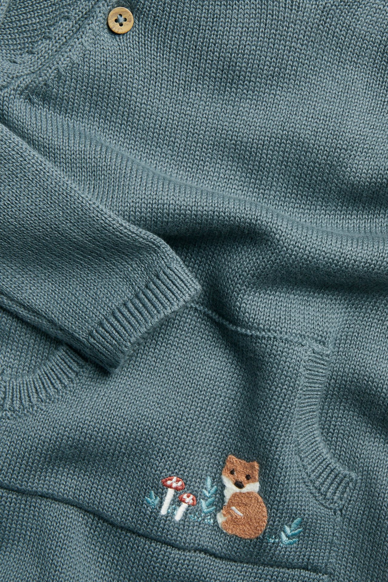 Nahaufnahme eines tealfarbenen gestrickten Baby Cardigans mit Knopf und Fuchs-Stickerei.