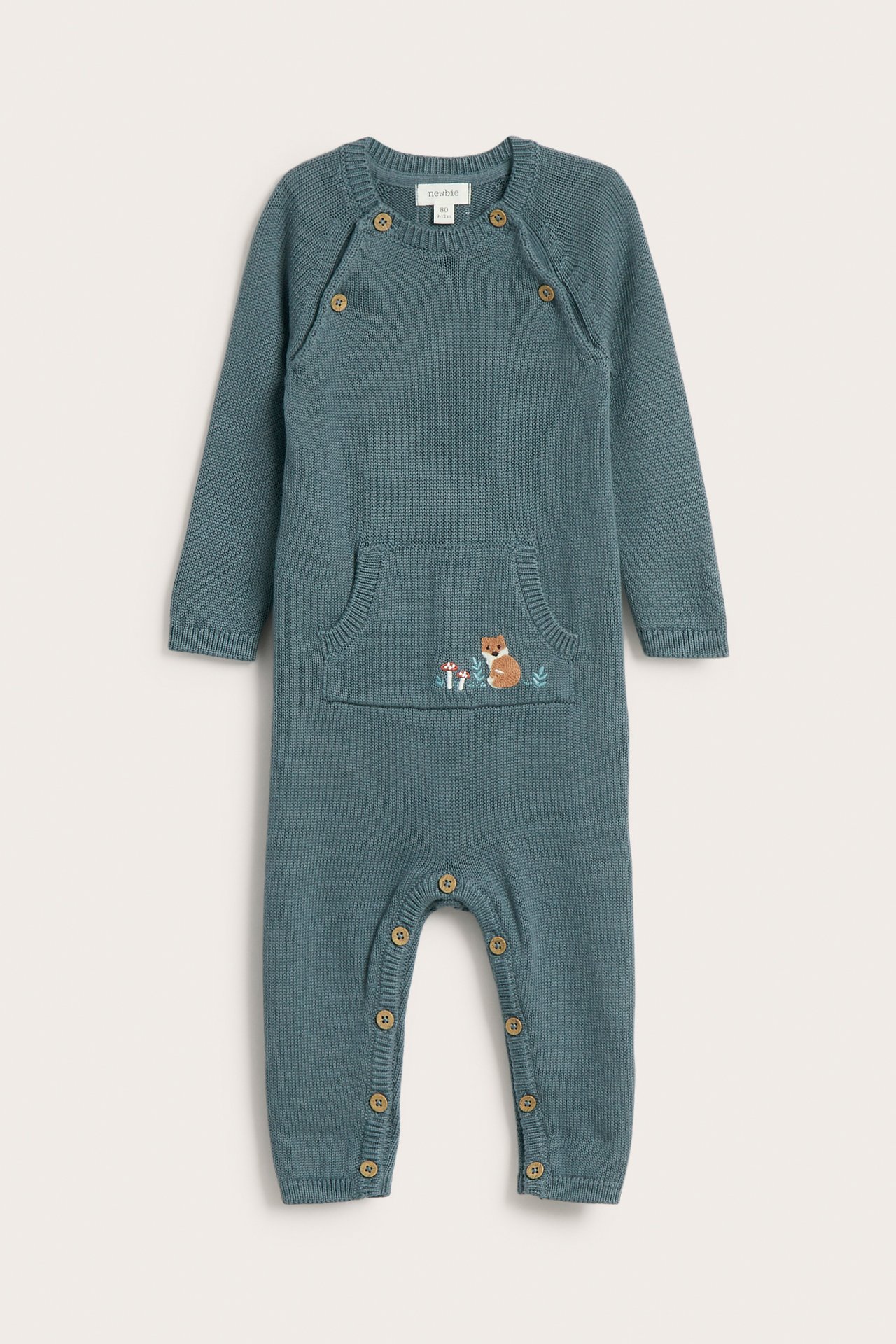 Front view of a baby's knitted teal long-sleeved jumpsuit with buttons and an embroidered fox pocket.
