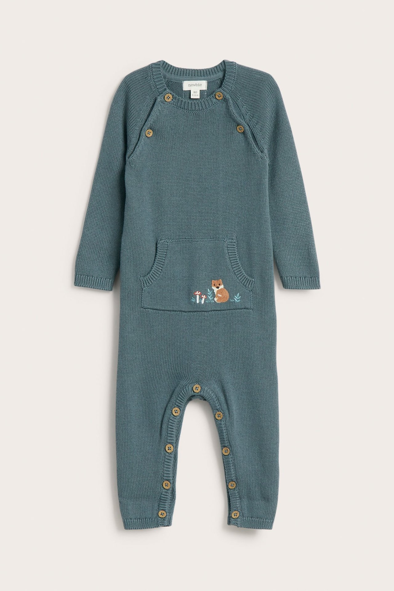 Vorderansicht eines gestrickten Baby-Overalls in Petrolblau mit Knöpfen und bestickter Fuchstasche.