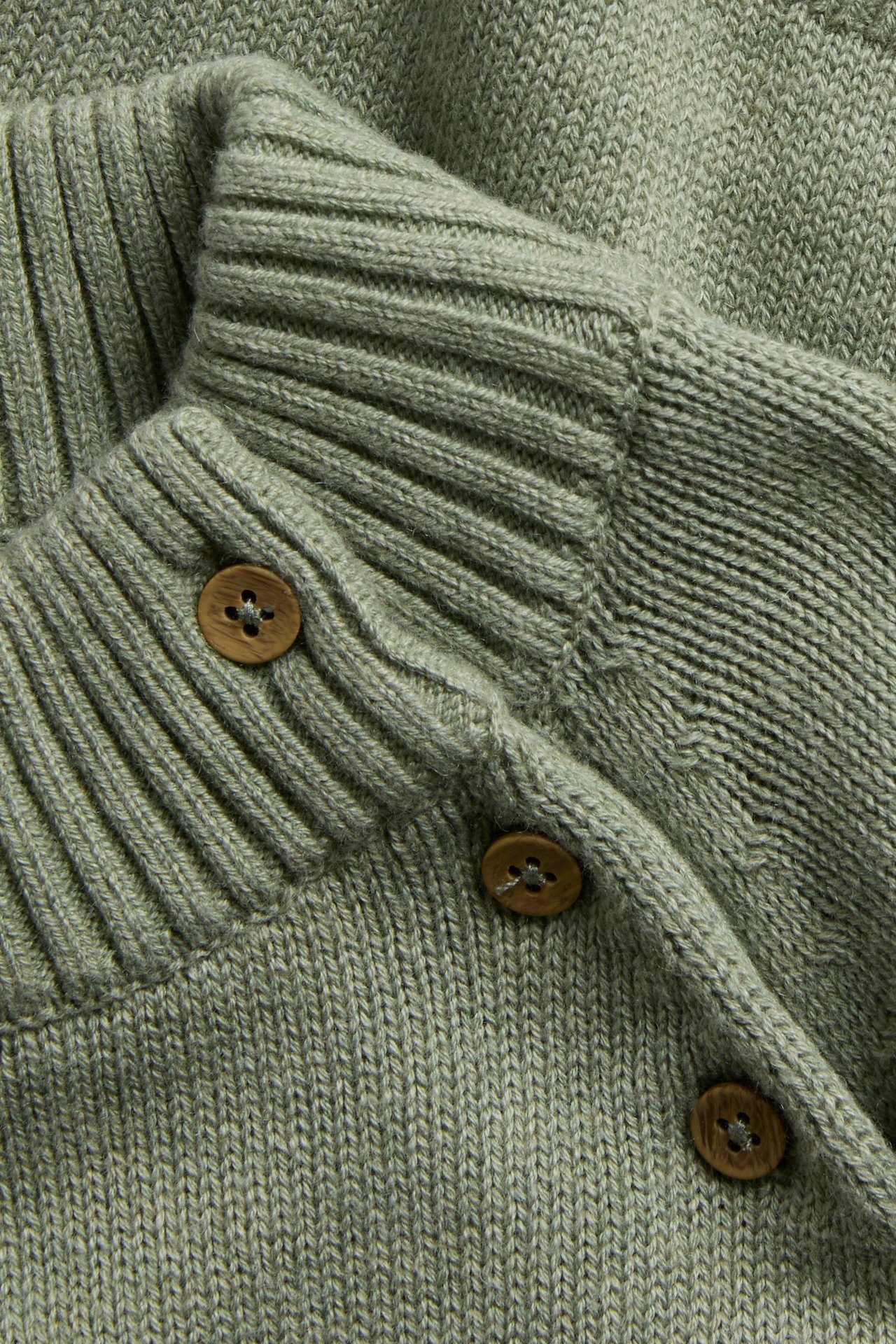 Nahaufnahme einer hellgrünen Strickjacke mit Rippdetails und drei braunen Holzknöpfen.