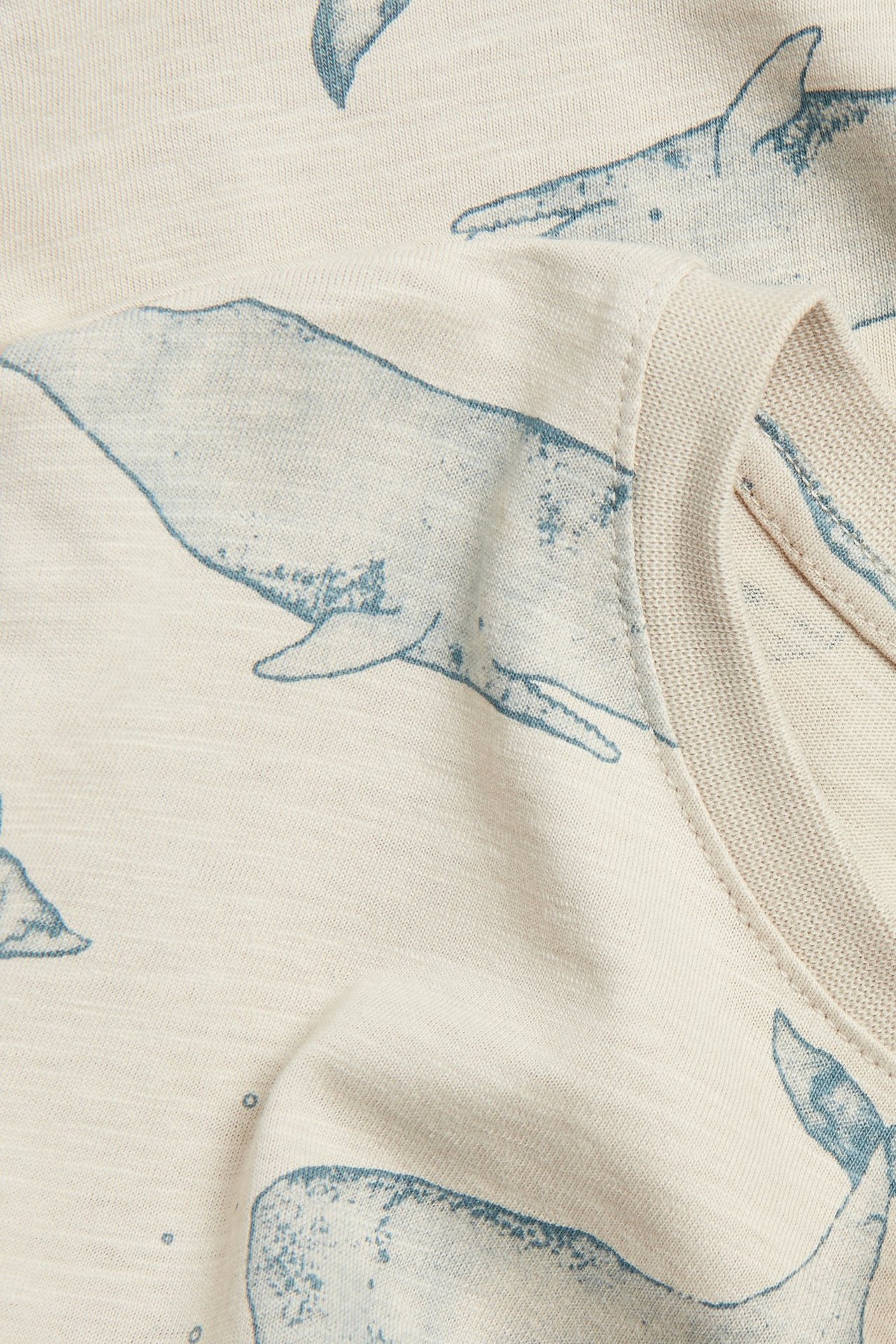 Nahaufnahme eines beigen Slub-T-Shirts mit blauem Walmuster und Ripphalsausschnitt.