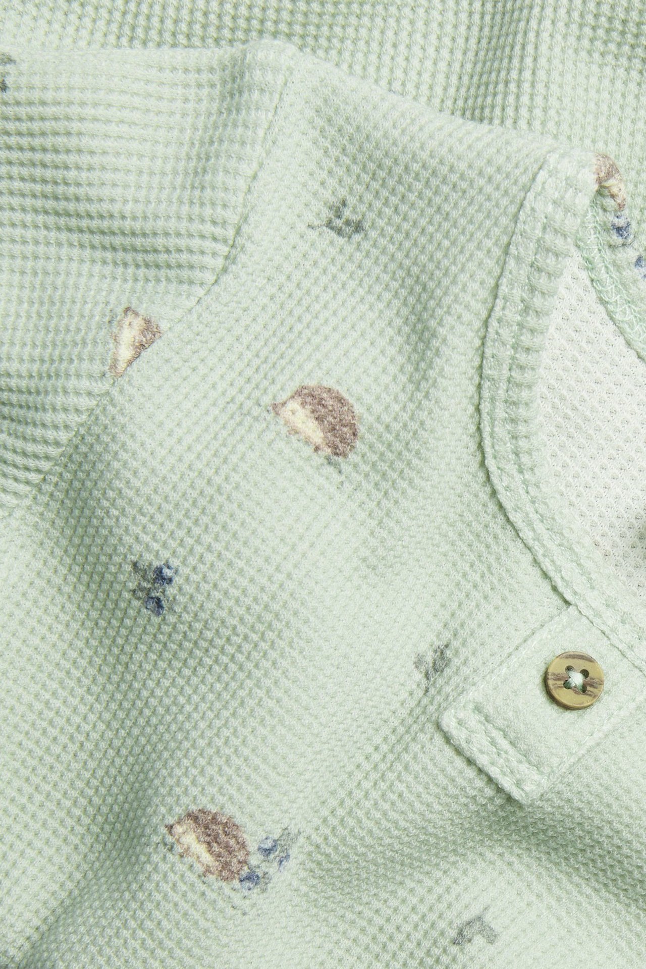 Nahaufnahme eines grünen langärmeligen Waffel-Bodys mit Igelmuster und einem dekorativen Holzknopf.