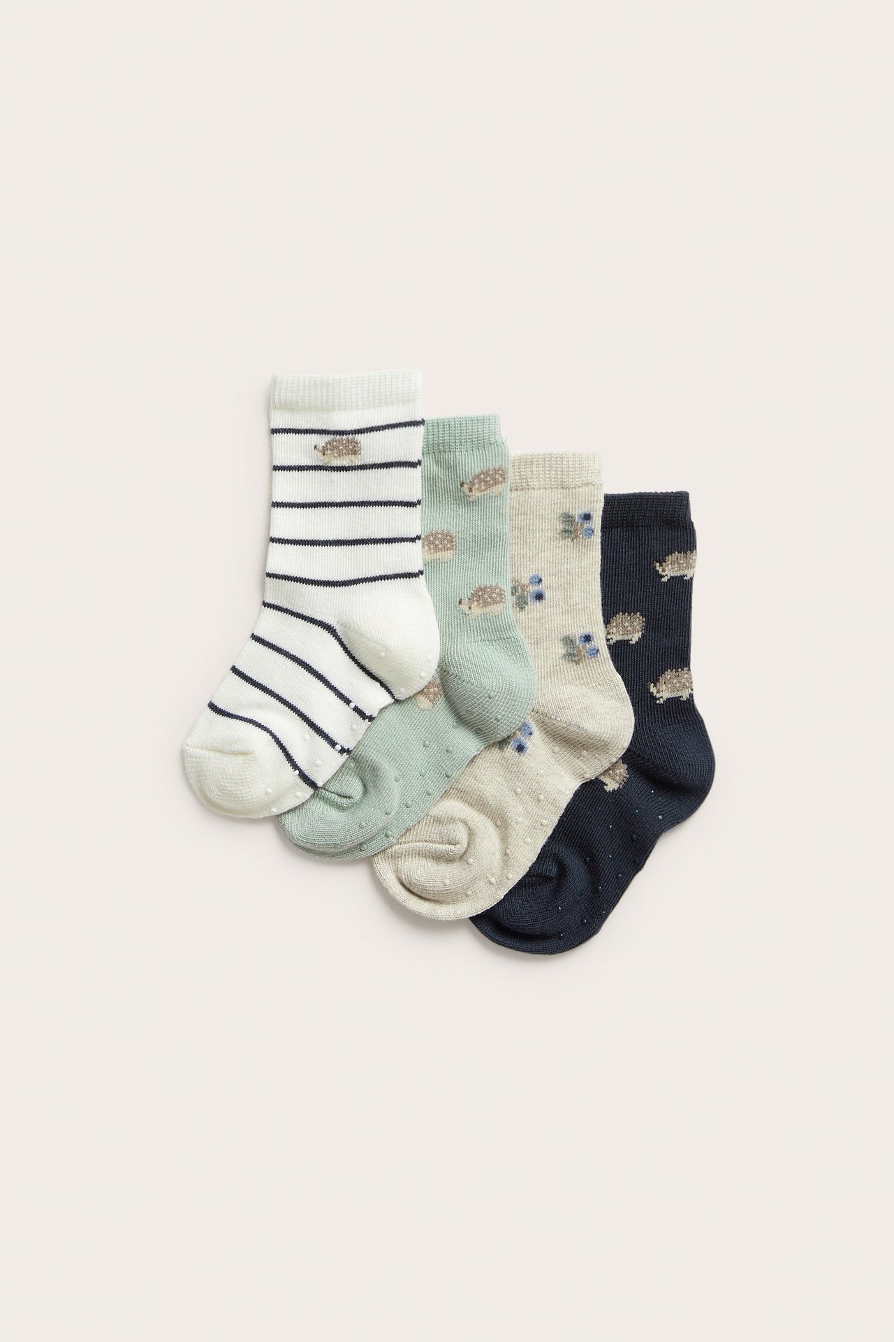 Draufsicht: Vier gemusterte Babysocken; gestreift, mintgrün, beige, dunkelblau, mit Igeln, Blaubeeren und Anti-Rutsch-Sohlen.