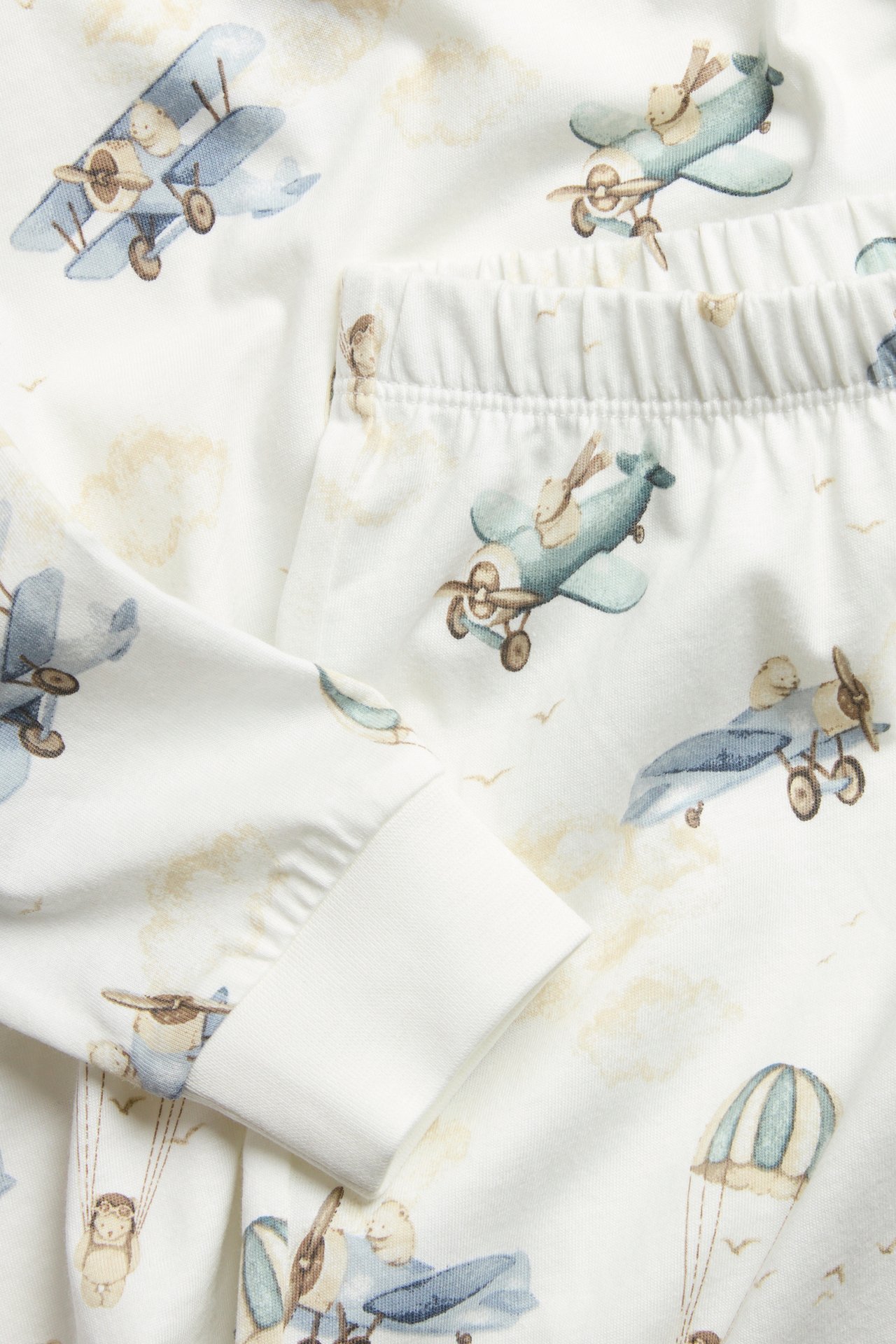 Close-up of off-white two-piece kid's pyjamas in soft jersey, with all-over teddy bear and airplane print.