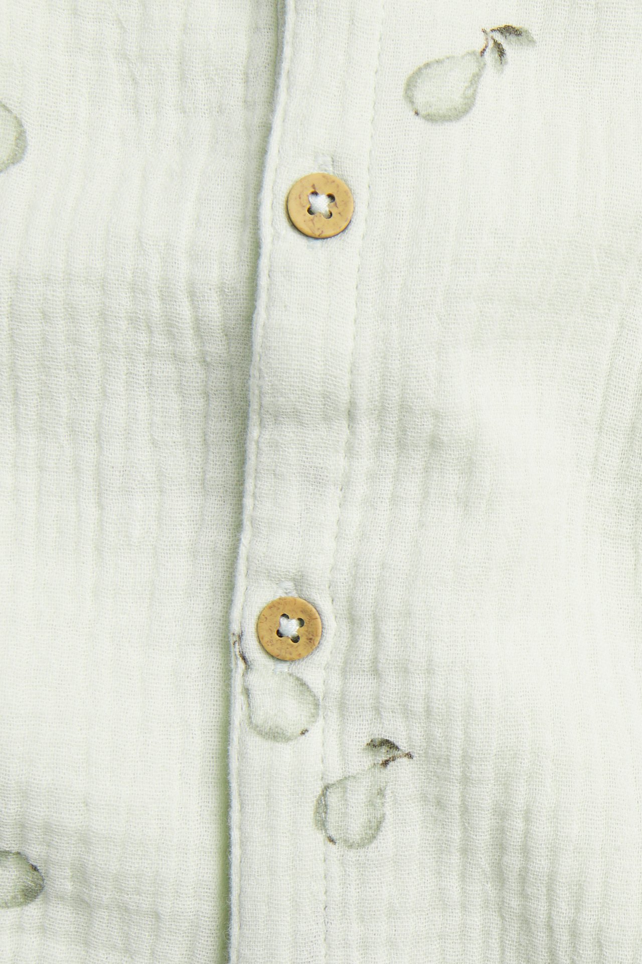 Close-up of a light green woven cotton romper with a subtle pear pattern and visible wooden buttons.