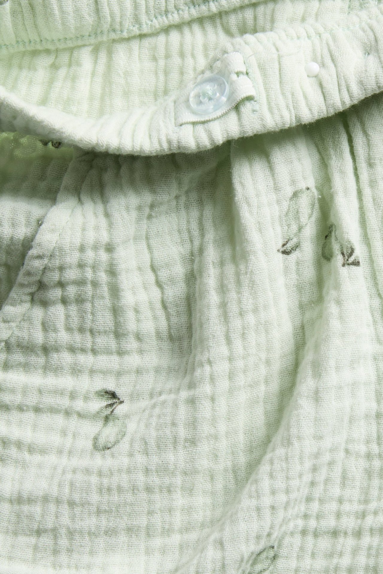 Nahaufnahme: hellgrüne Baumwoll-Musselin-Shorts mit Birnenmuster und Zierknopf am Gummibund.