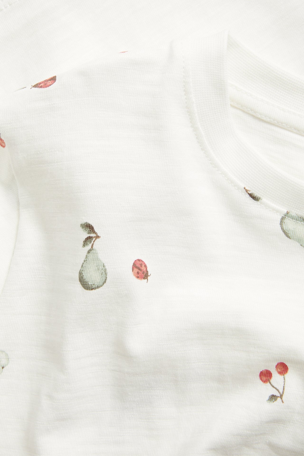 Nahaufnahme: Off-weißes Slub-Baumwoll-T-Shirt mit Birnen-, Kirsch- und Marienkäfer-Muster.