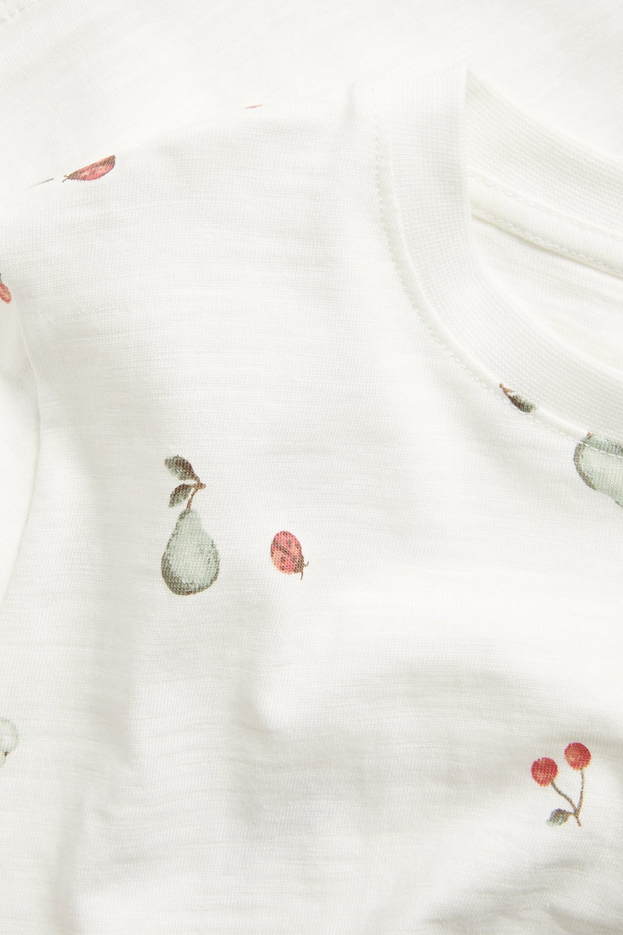 Nahaufnahme: Off-weißes Slub-Baumwoll-T-Shirt mit Birnen-, Kirsch- und Marienkäfer-Muster.