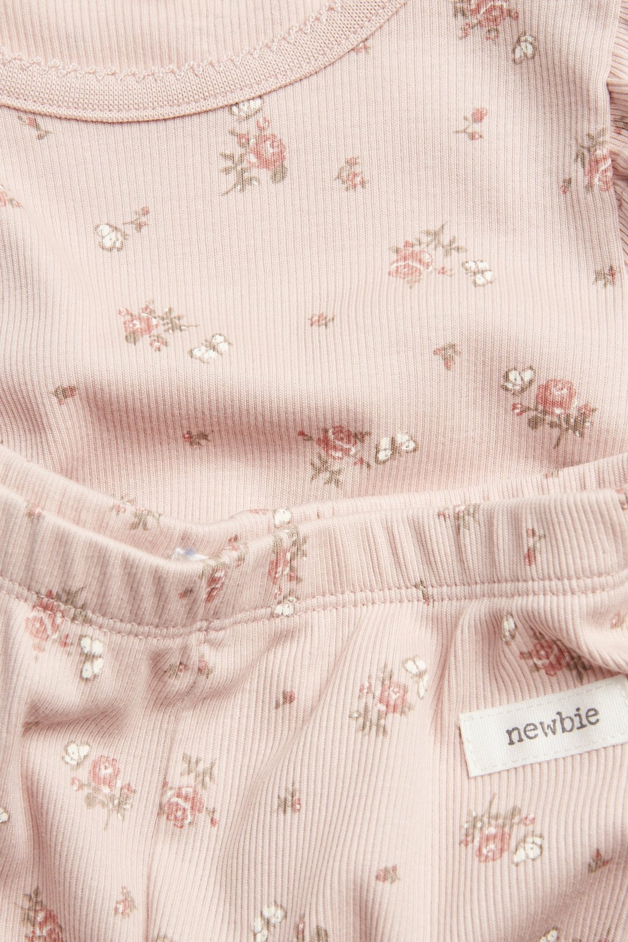 Nahaufnahme, Vorderansicht, eines rosa gerippten zweiteiligen Baby-Pyjamas aus Baumwolle mit Blumen- und Schmetterlingsmuster.