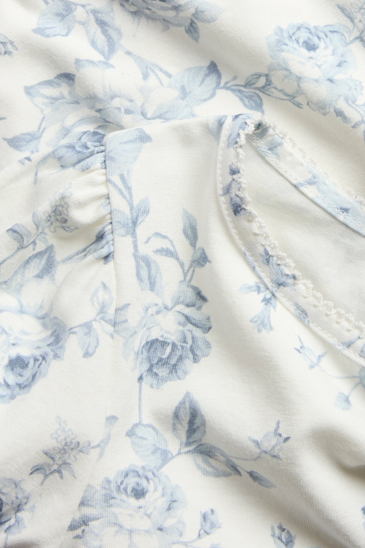 Close-up of an off-white floral jersey top with ruffled puff sleeves and picot trim.