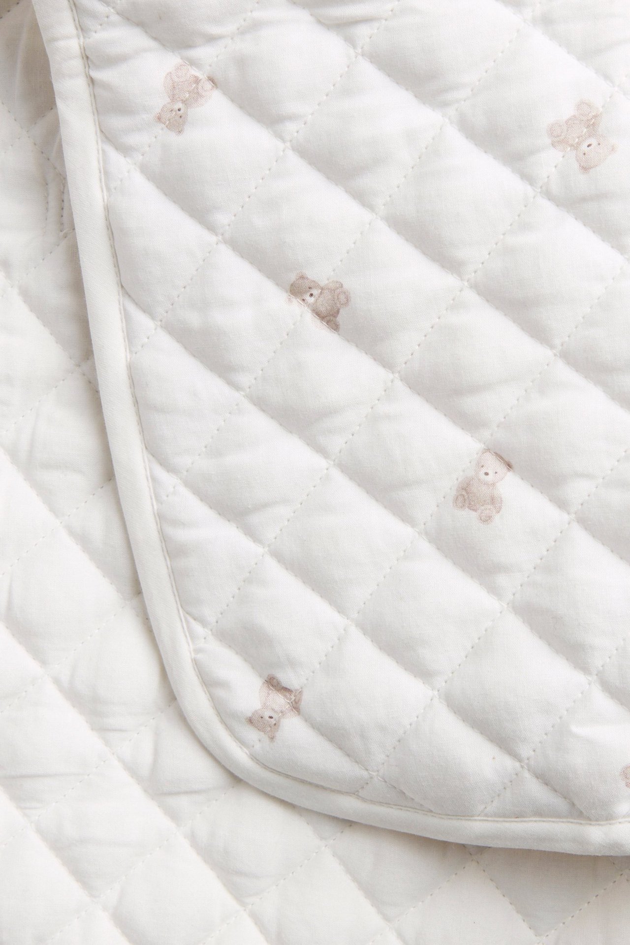 Close-up of an off-white quilted changing mat with a small brown teddy bear pattern.