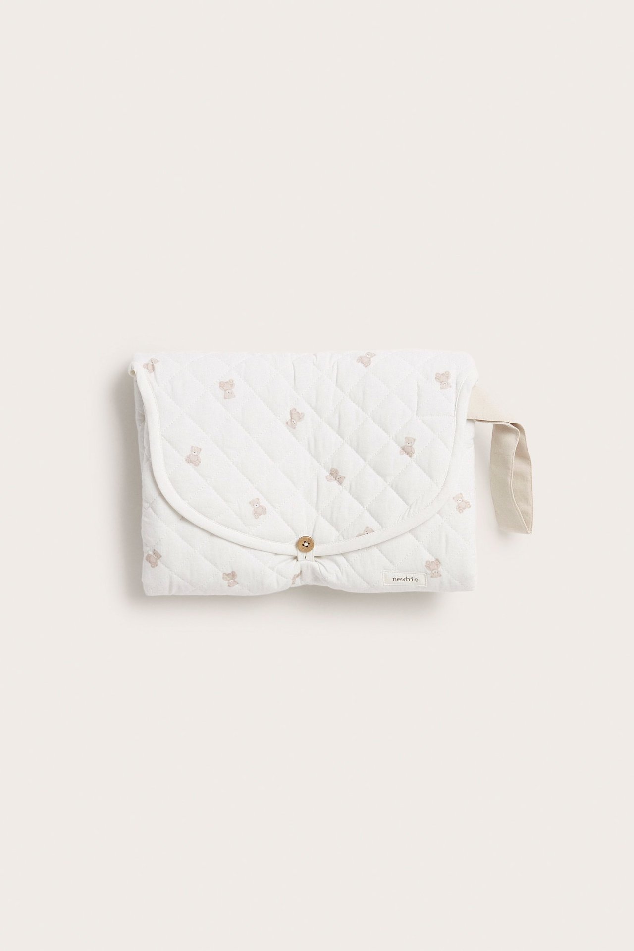 Front view of an off-white quilted foldable changing pad with teddy bear print, button closure, and handle.