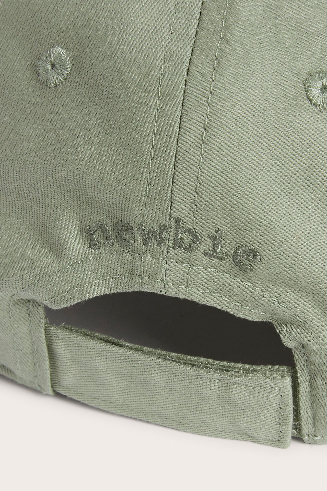 Close-up back view of a dark green cap with embroidered 'Newbie' text and an adjustable strap.