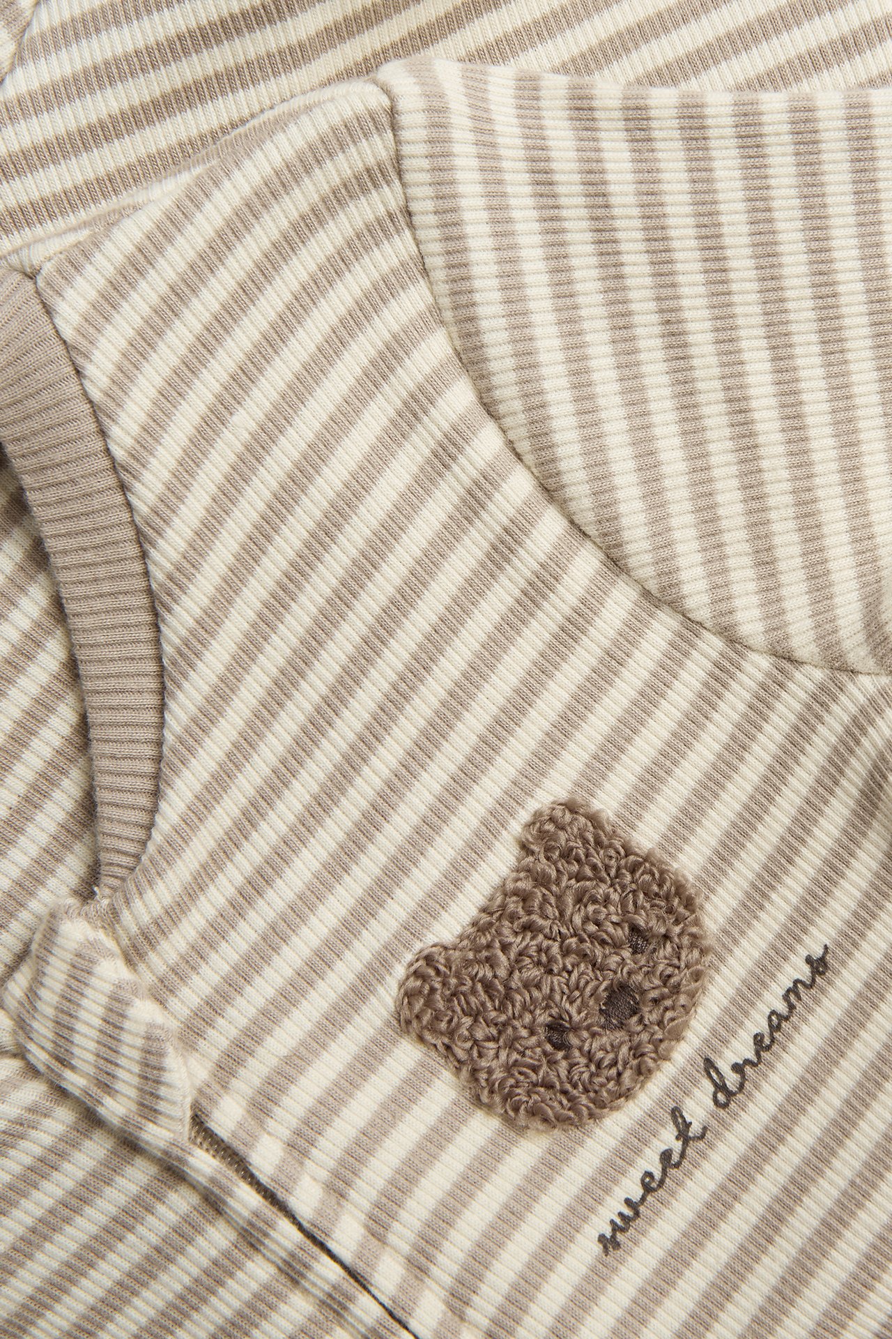 Close-up of a striped beige baby pyjamas in ribbed jersey with a teddy bear application and "sweet dreams".