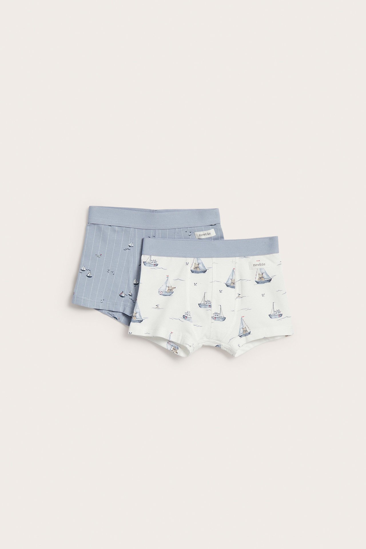 Vorderansicht: Zwei Kinder-Boxershorts. Eine weiße mit blauen Segelbooten, eine hellblaue mit Streifen.