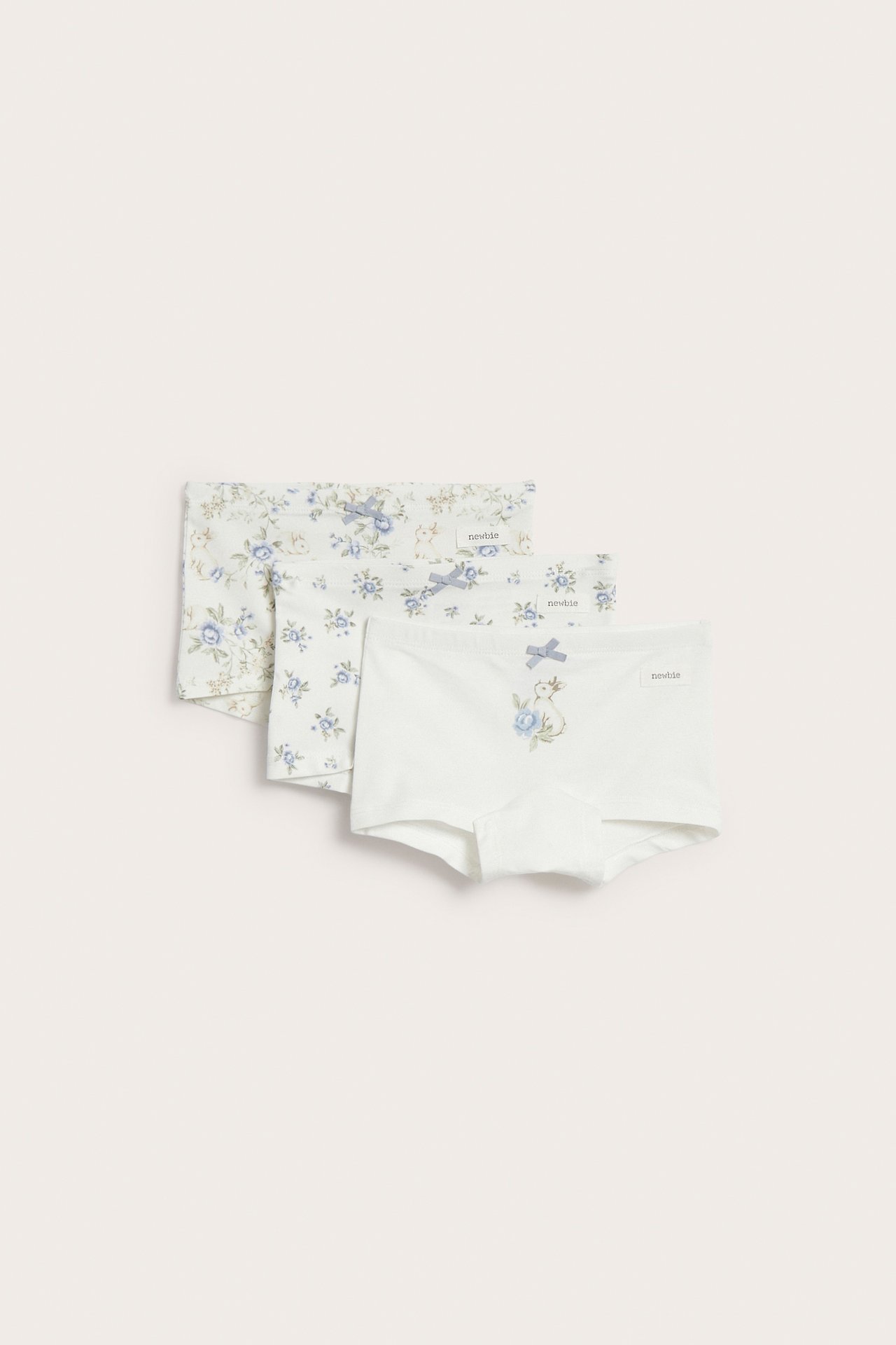Front view of three off-white kid's boxer briefs, blue floral and rabbit patterns, each with a bow.