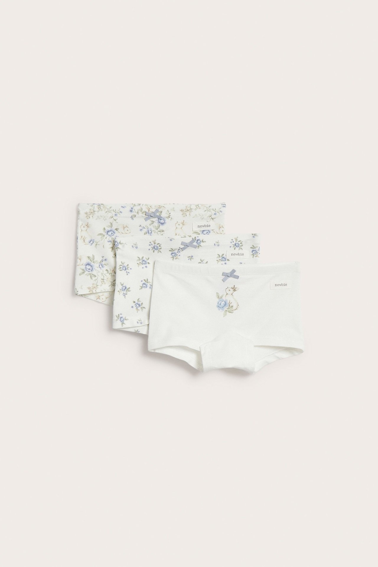 Front view of three off-white kid's boxer briefs, blue floral and rabbit patterns, each with a bow.