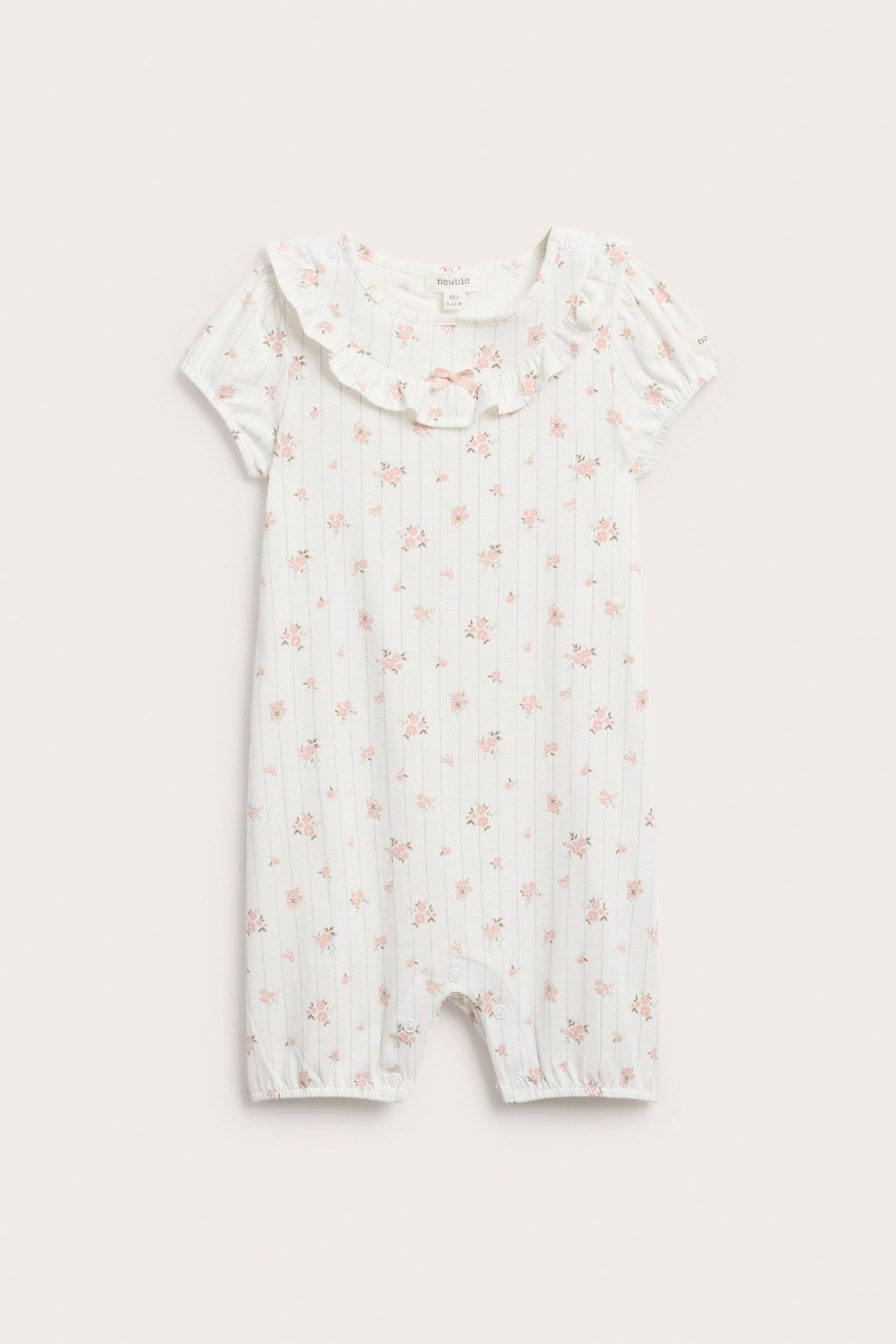 Vorderansicht: Off-white Baby-Strampler, rosa Blumenmuster, Rüschenausschnitt, kurze Ärmel, Druckknöpfe.