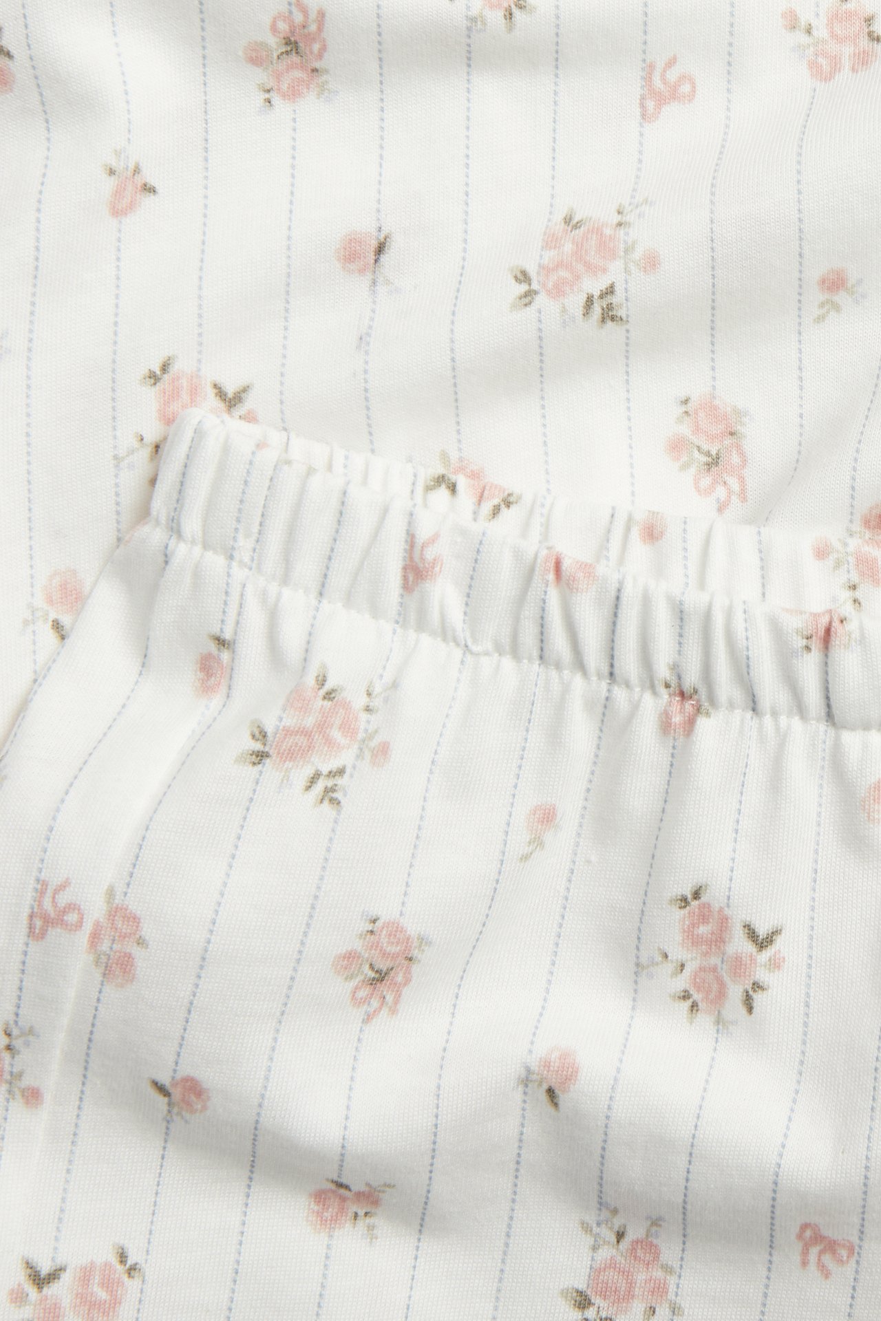 Close-up of an off-white cotton pyjama with pink floral pattern, thin blue stripes, and an elastic waistband.