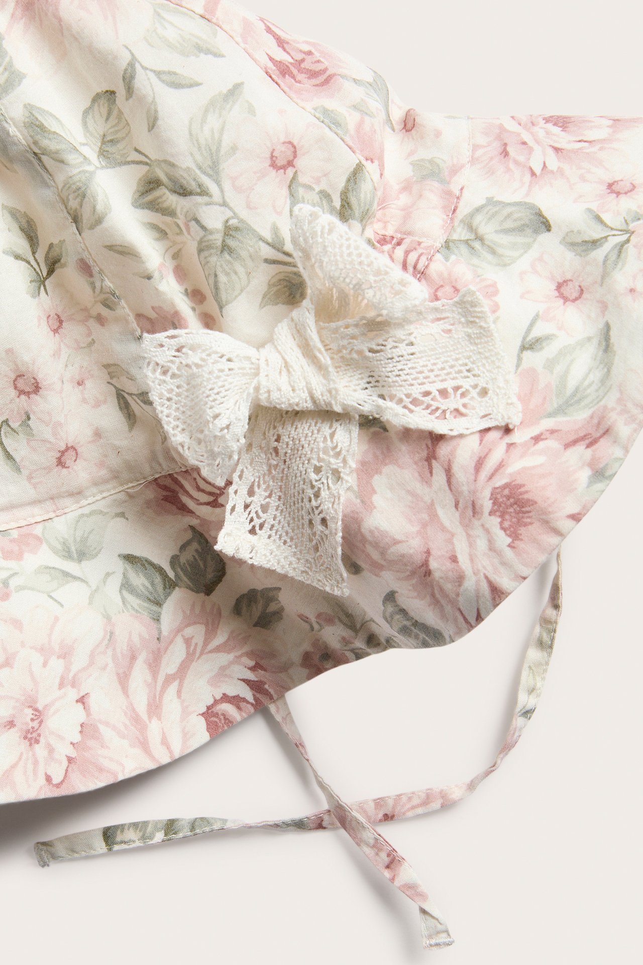 Close-up of an off-white baby floral sun hat with a lace bow detail and tie bands.