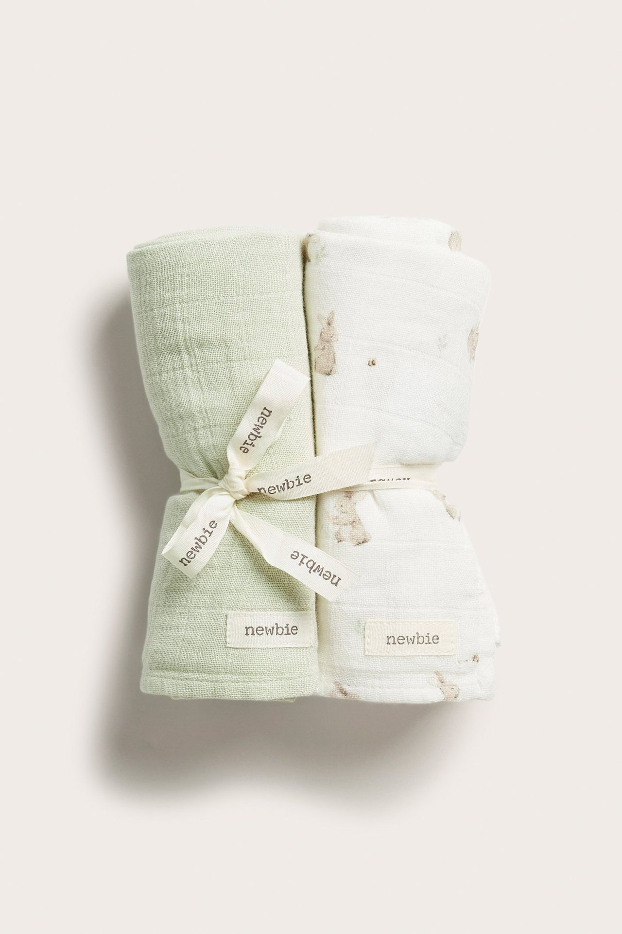 Front view of two rolled muslin blankets: light green and off-white with bunny pattern, tied with a ribbon.
