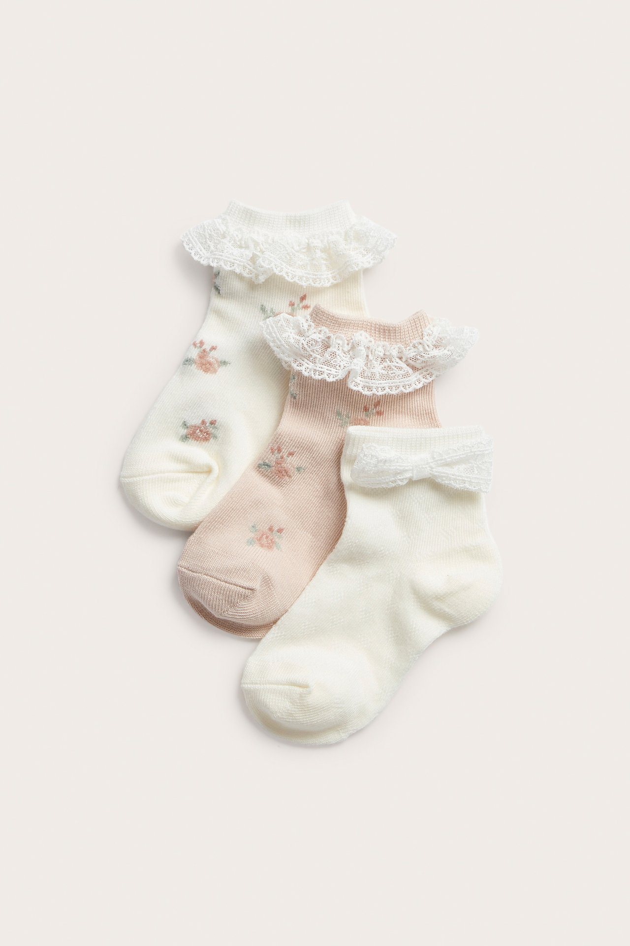 Top-down view of three baby socks: two floral with lace, one off-white pointelle with bow.