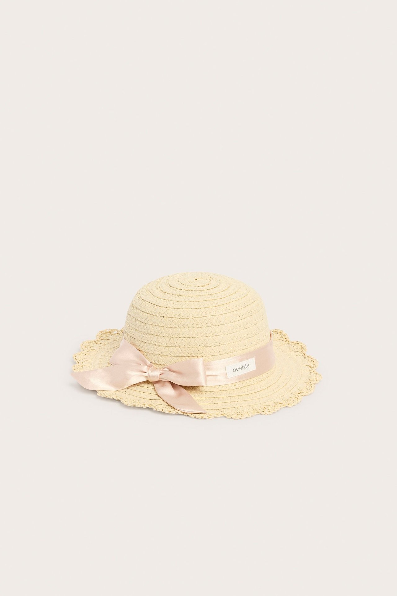Front view of a light beige straw hat with a pink satin bow and a scalloped brim.