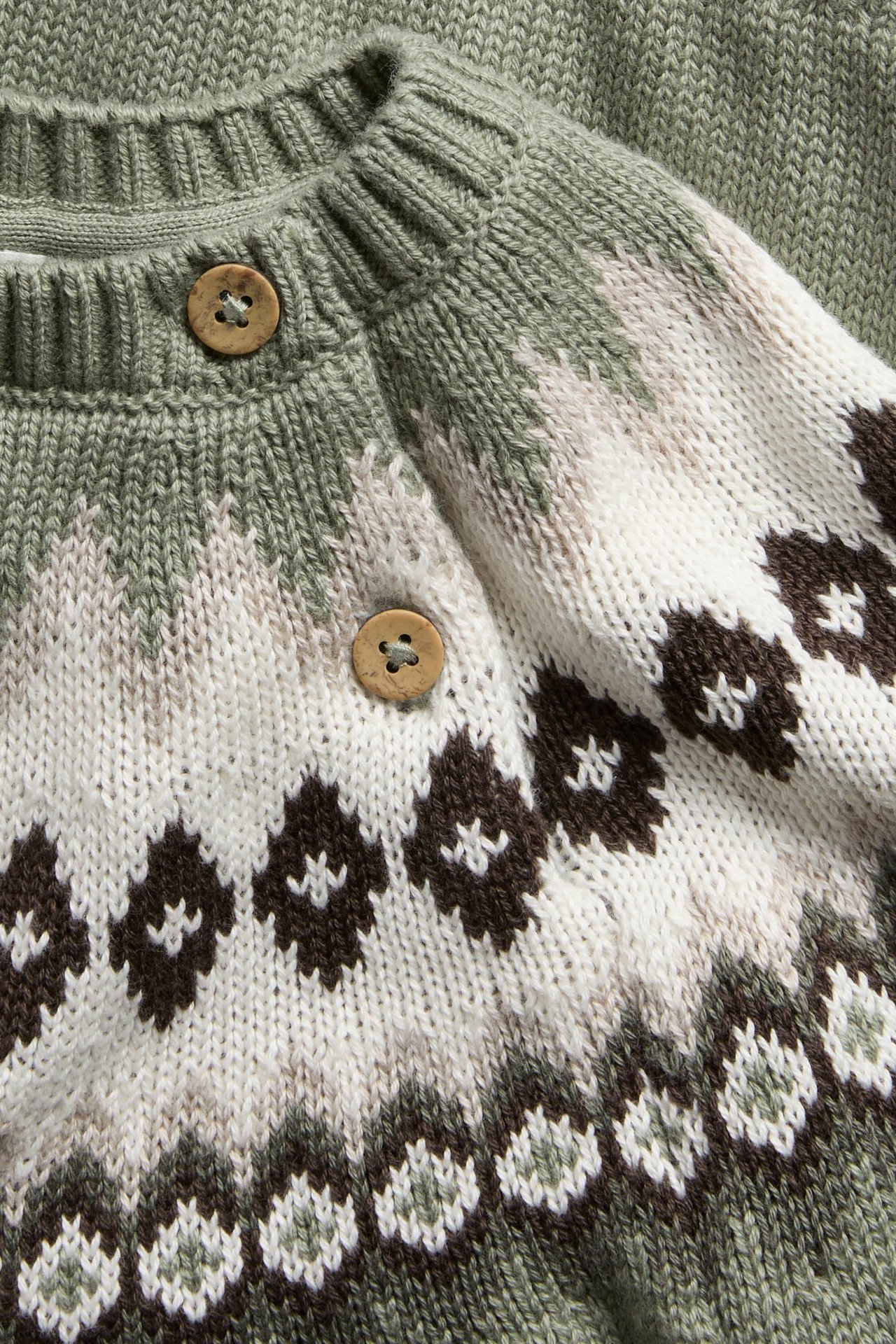 Nahaufnahme einer Baby-Fair-Isle-Strickjacke in Salbeigrün, Weiß, Braun, mit zwei Holzknöpfen.