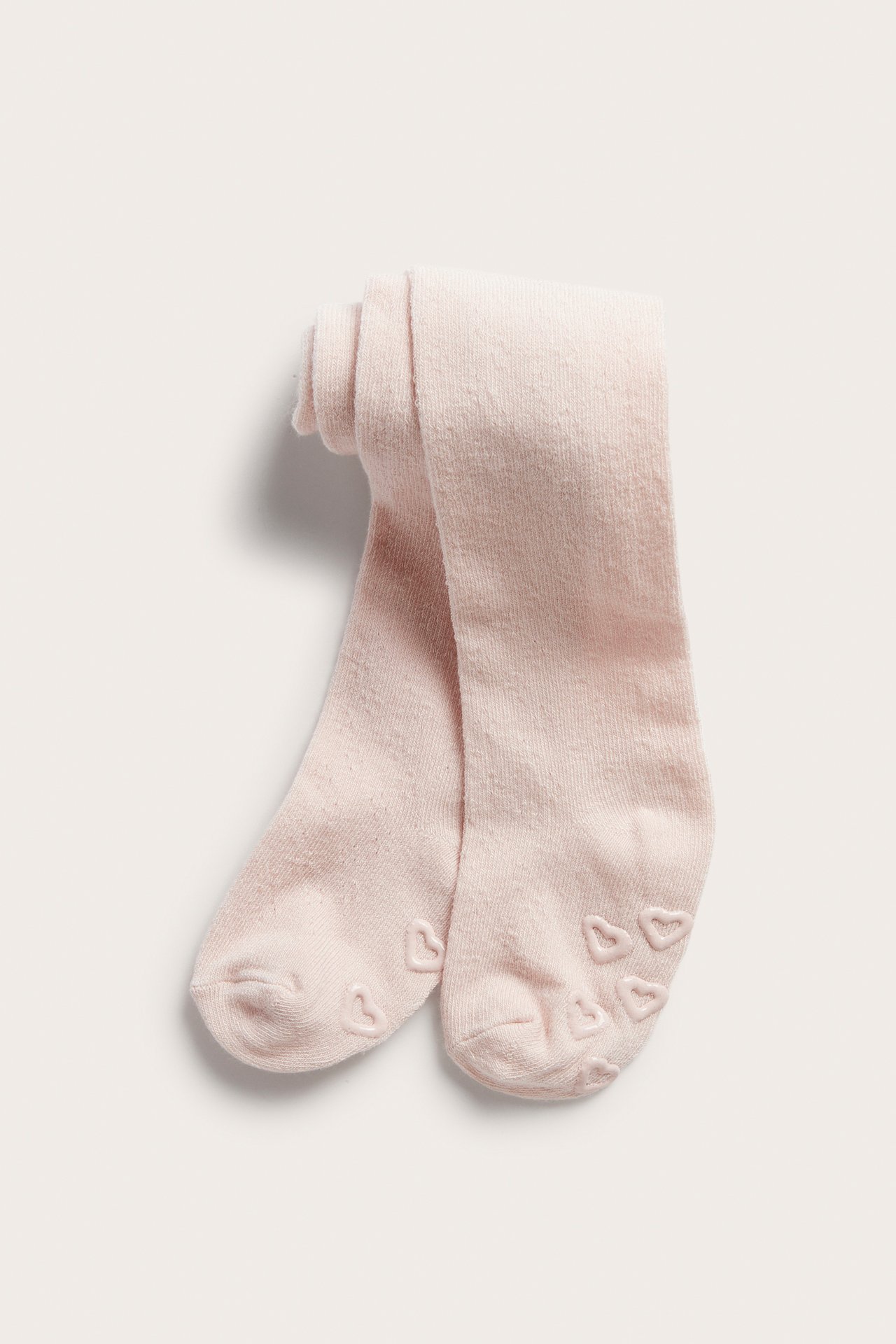 Folded light pink baby tights with anti-slip heart patterns on the soles.