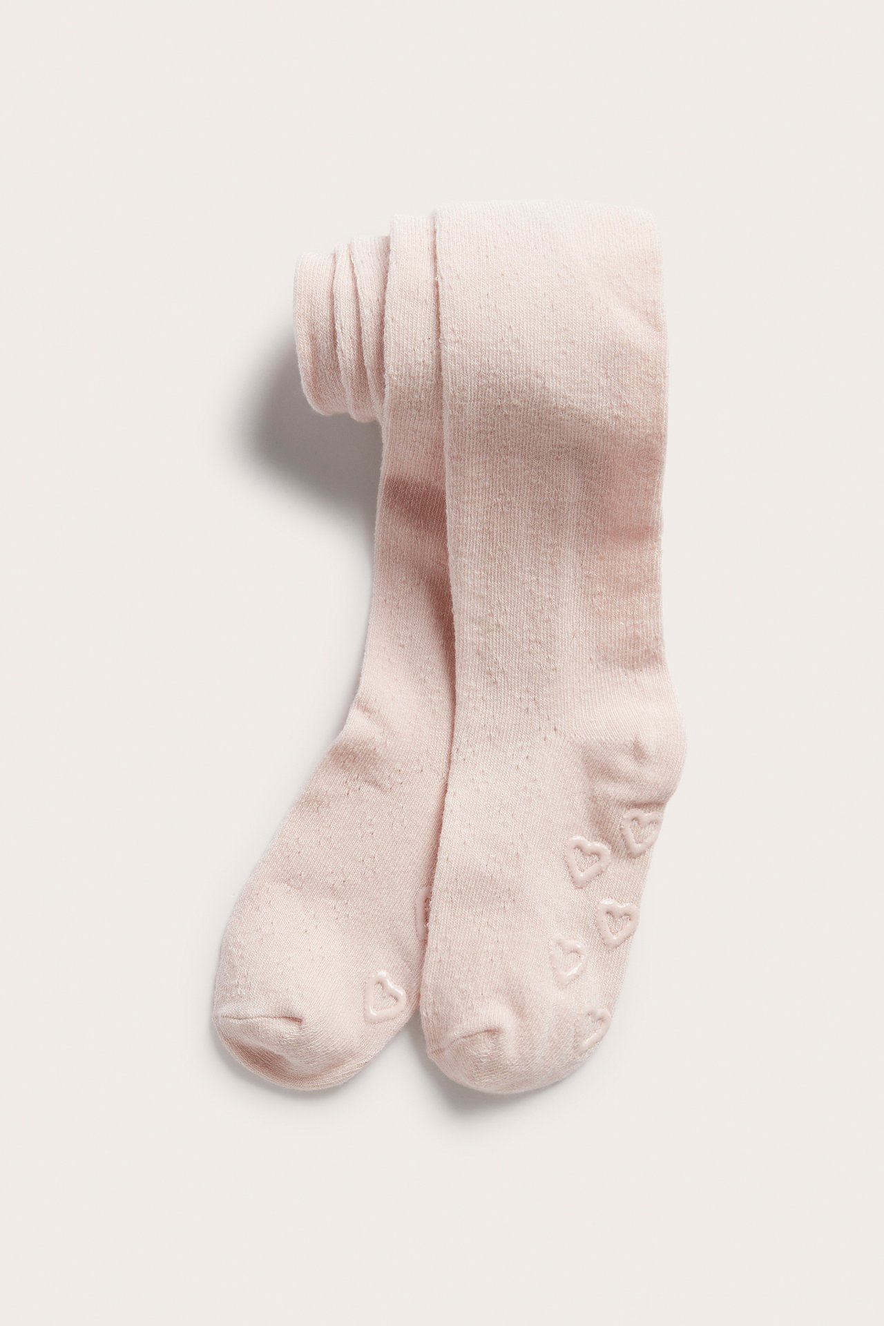 Front view of folded light pink knitted baby tights with a subtle hole pattern and heart anti-slip soles.