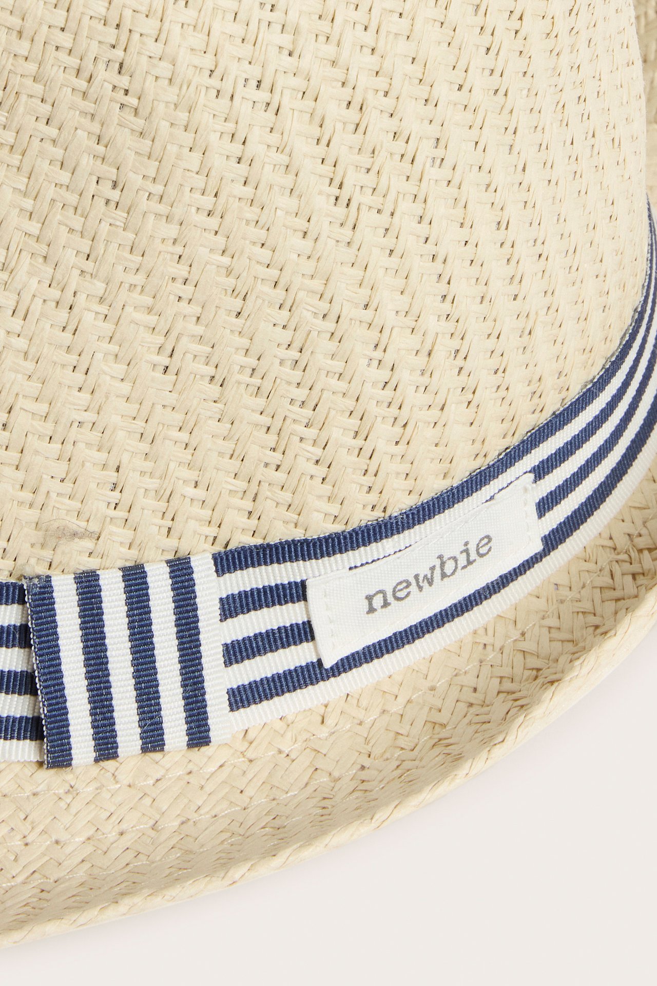 Close-up of a light beige straw hat for kids with a blue and white striped band and a Newbie label.