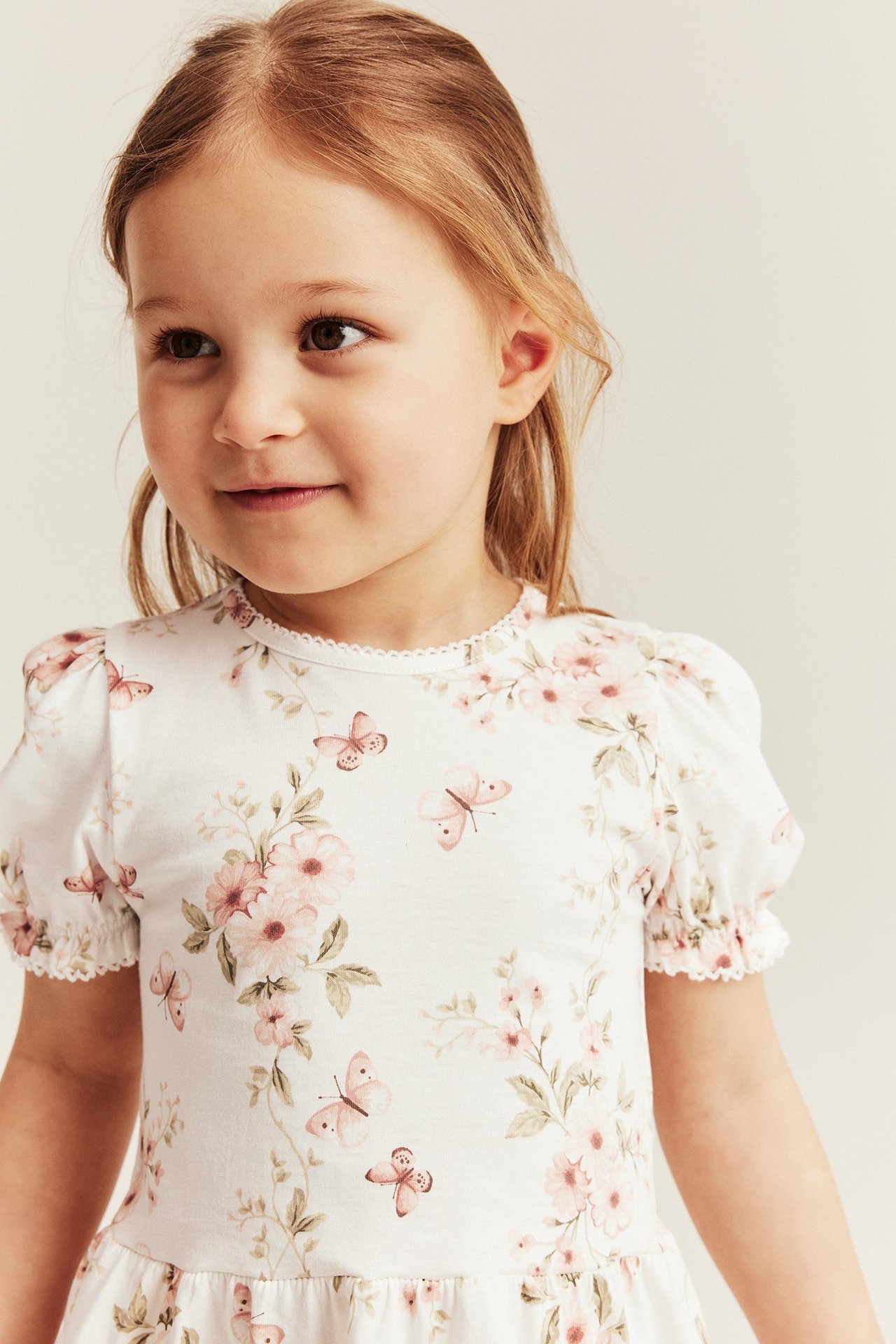 Front view of a kid in an offwhite peplum top with pink floral and butterfly print, featuring puff sleeves.