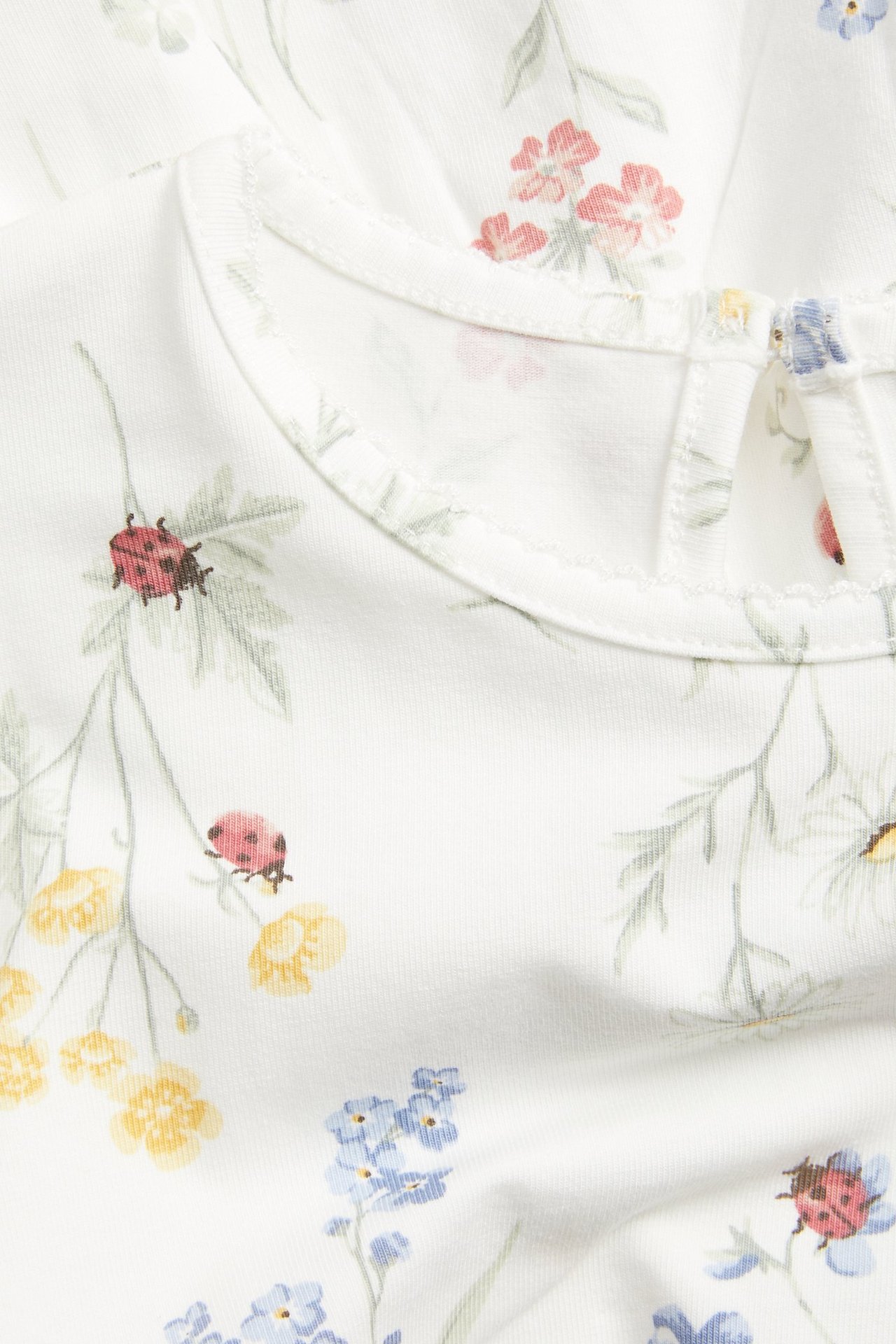 Nahaufnahme: cremeweißes florales Jersey-Peplum-Top mit Marienkäfern und Schlüssellochverschluss.