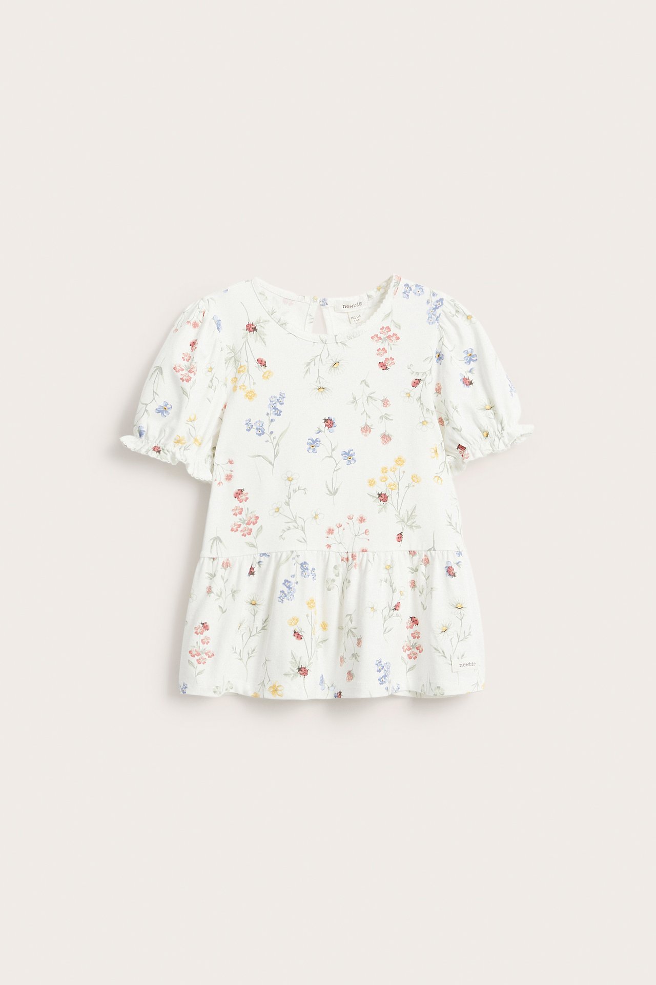 Front view of an off-white kid's peplum top with colorful floral and ladybug print, short puff sleeves.