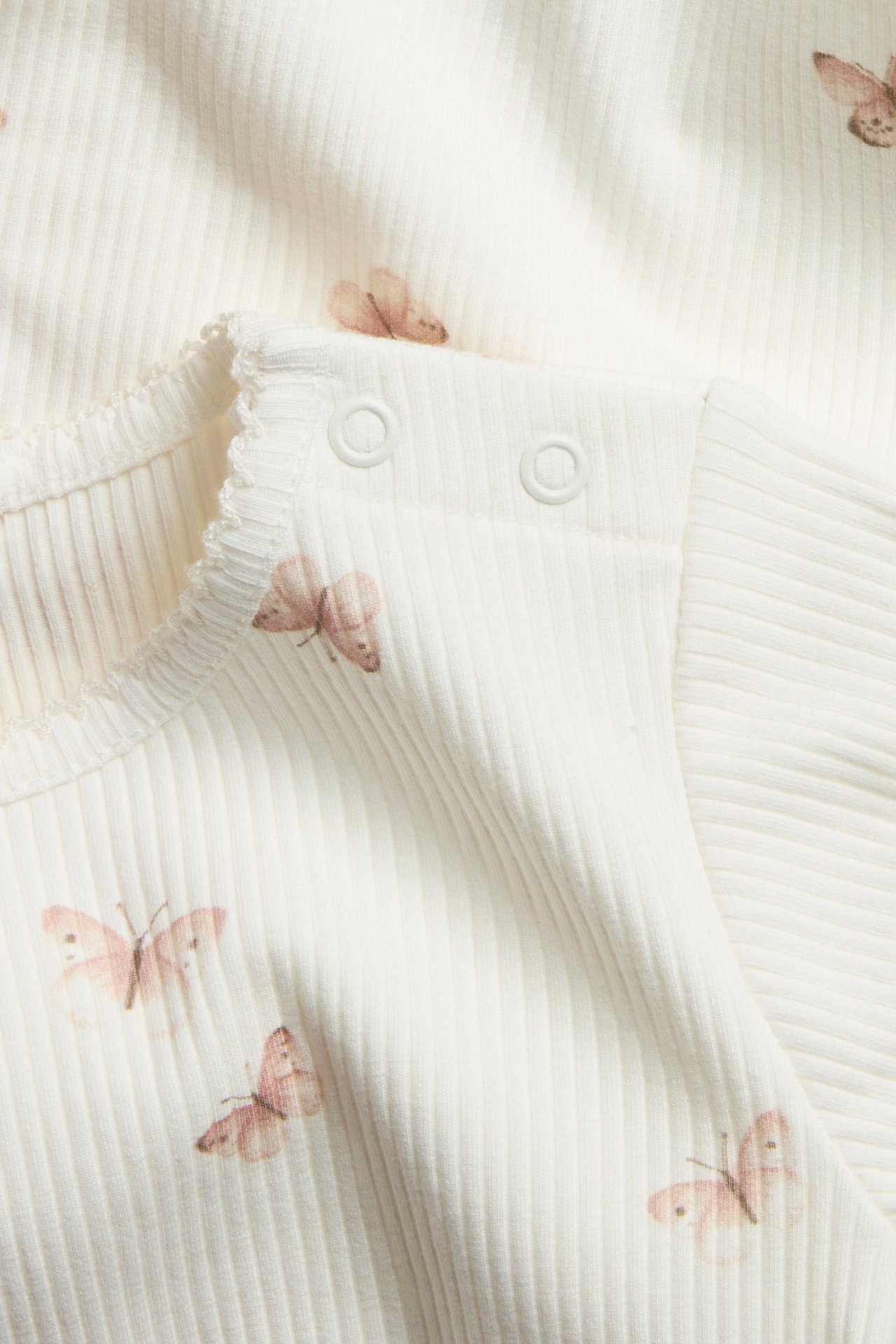 Close-up: off-white ribbed baby bodysuit with a pink butterfly pattern, snap fasteners on shoulder.