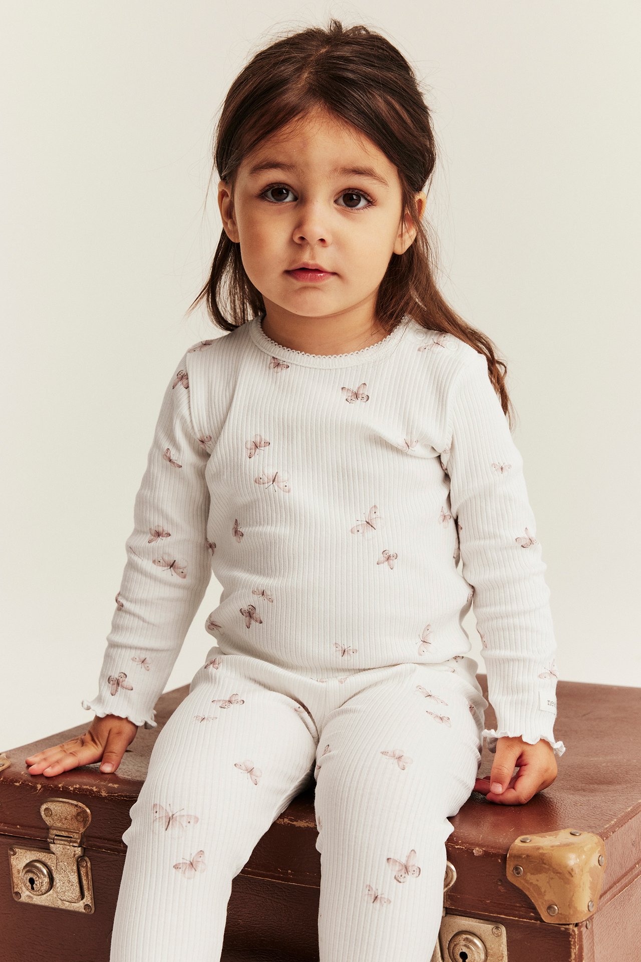Vorderansicht eines Kindes in einem cremefarbenen gerippten Langarm-Body mit Schmetterlingsmuster und passenden Leggings.
