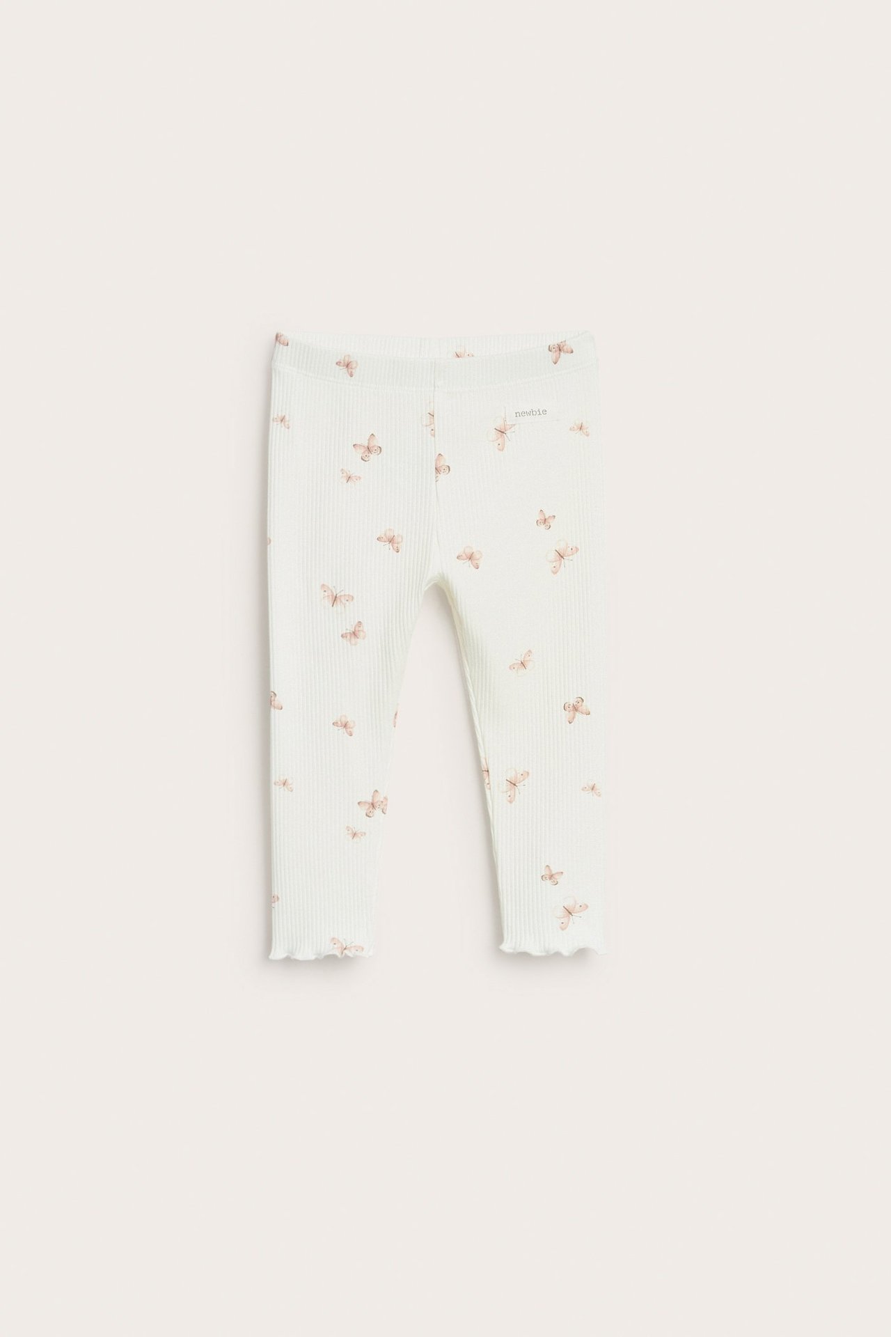 Vorderansicht: Baby-Leggings in Offwhite, gerippt, mit hellbraunem Schmetterlingsmuster und gewellten Säumen.