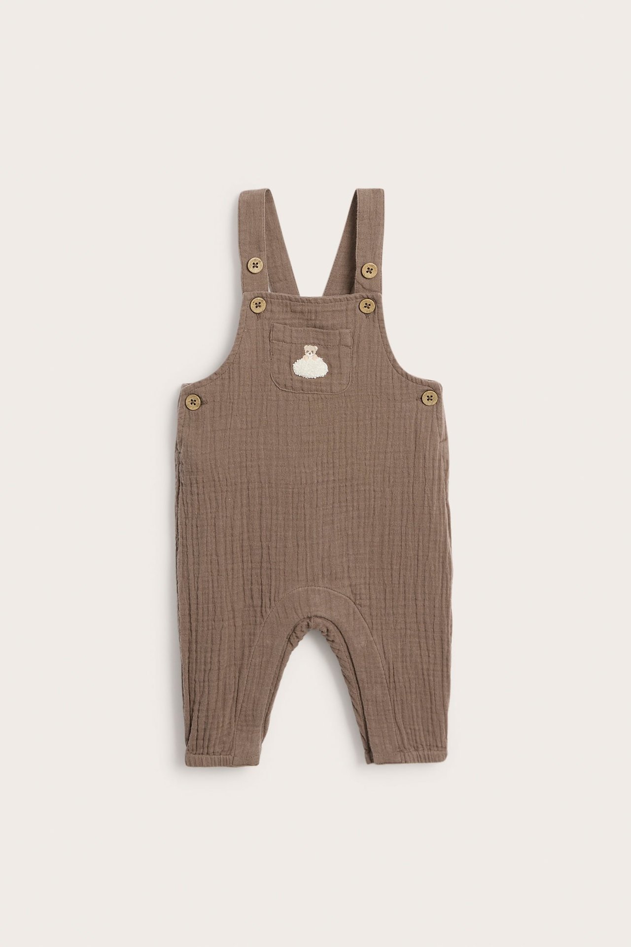 Front view of baby brown muslin dungarees with adjustable straps and a front pocket with cloud embroidery.