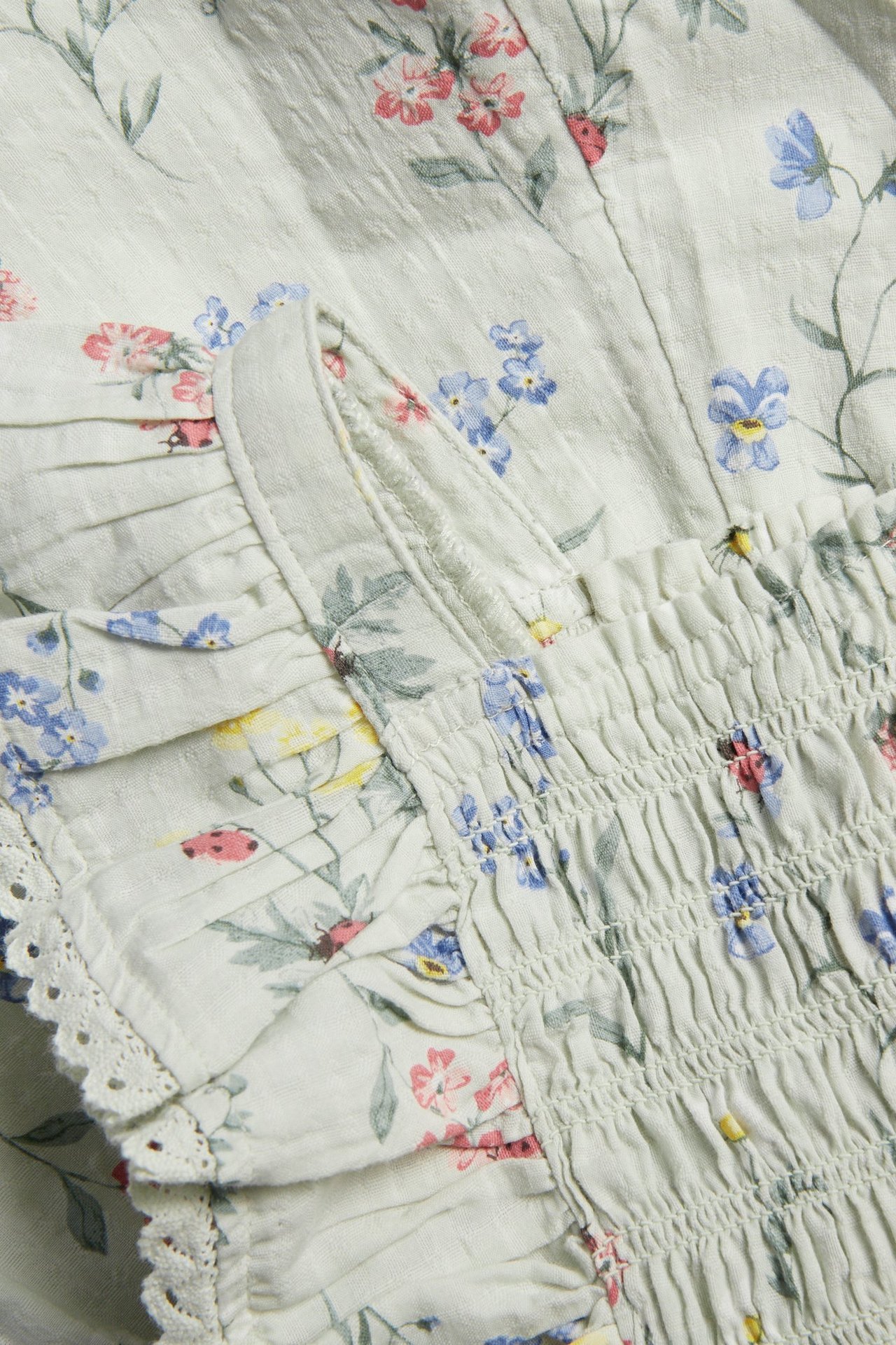 Close-up of a light green floral woven jumpsuit with smocked elastic, ruffles, and lace trim.