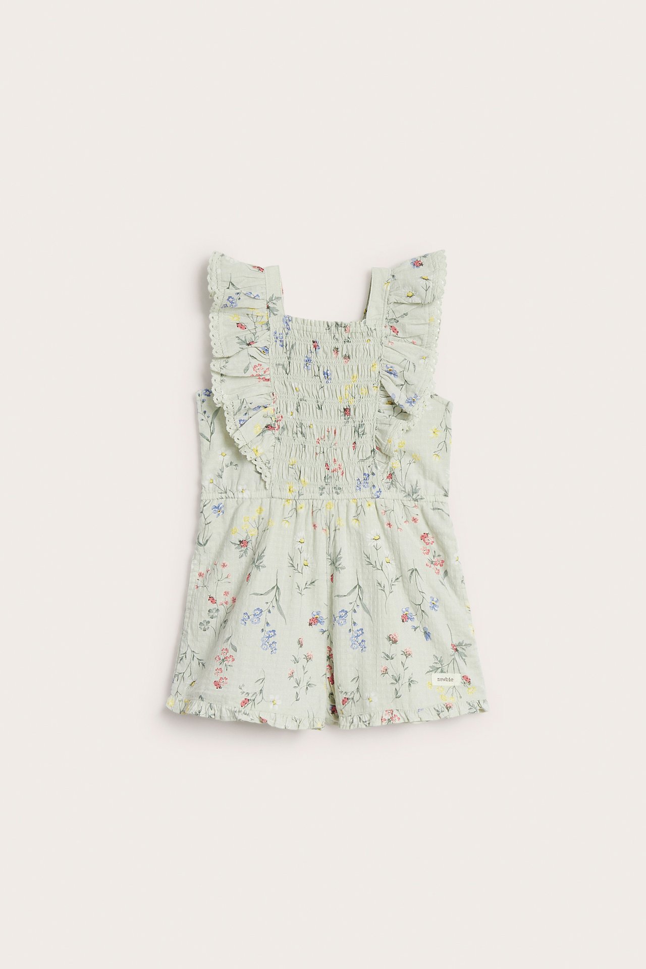 Front view of a kid's light green floral woven romper with ruffled straps and smocked bodice.